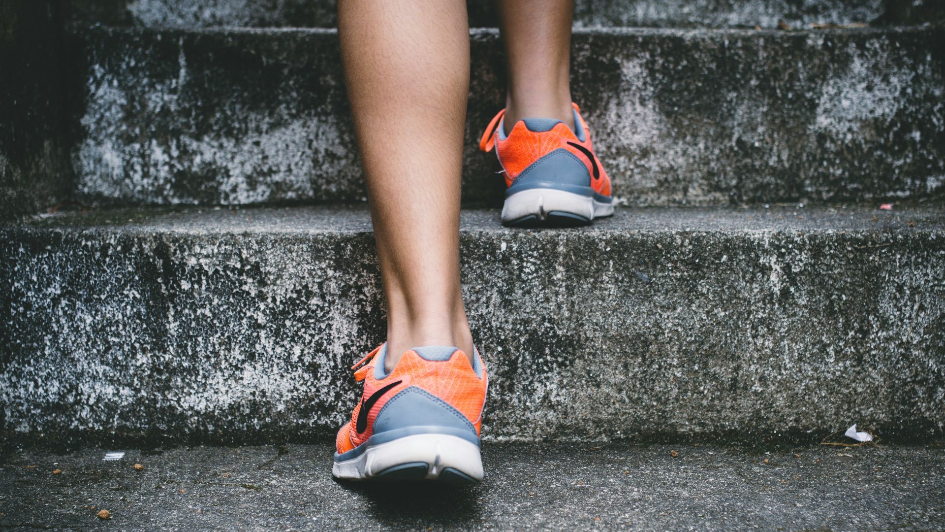 person wearing orange and gray Nike shoes walking on gray concrete stairs