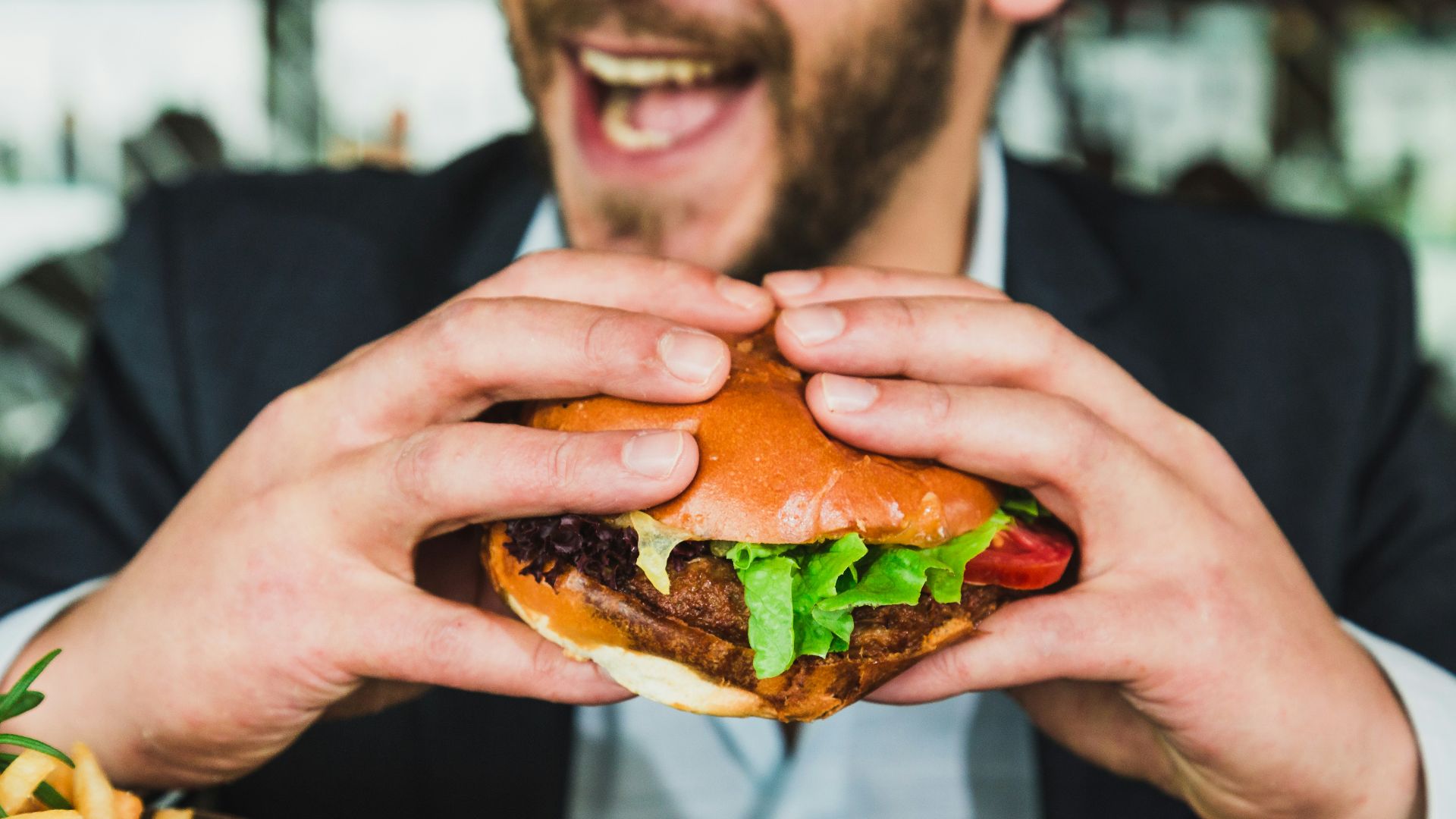 person holding burger bun with vegetables and meat