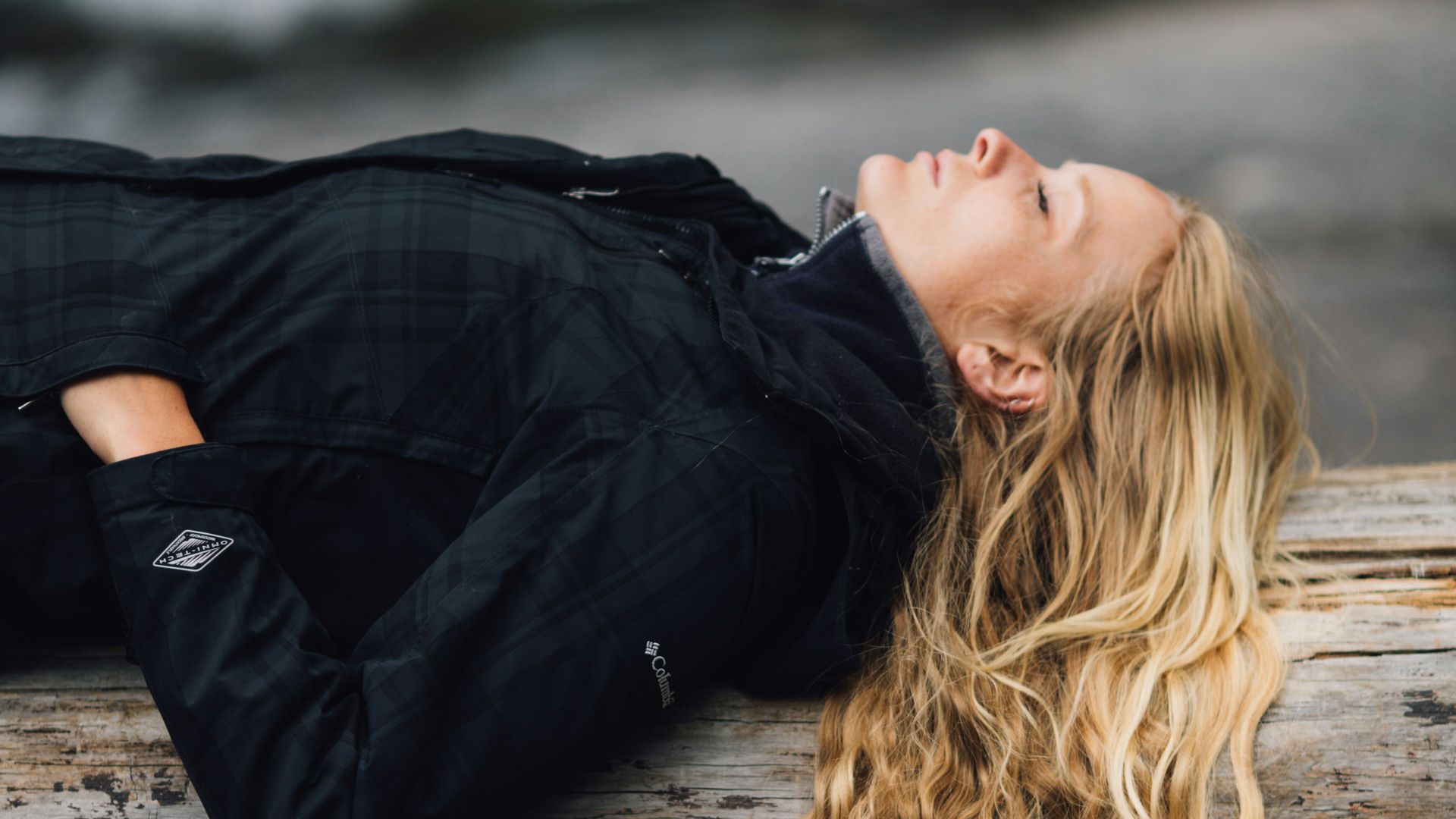 woman in black zip-up jacket leaning on large log at daytime