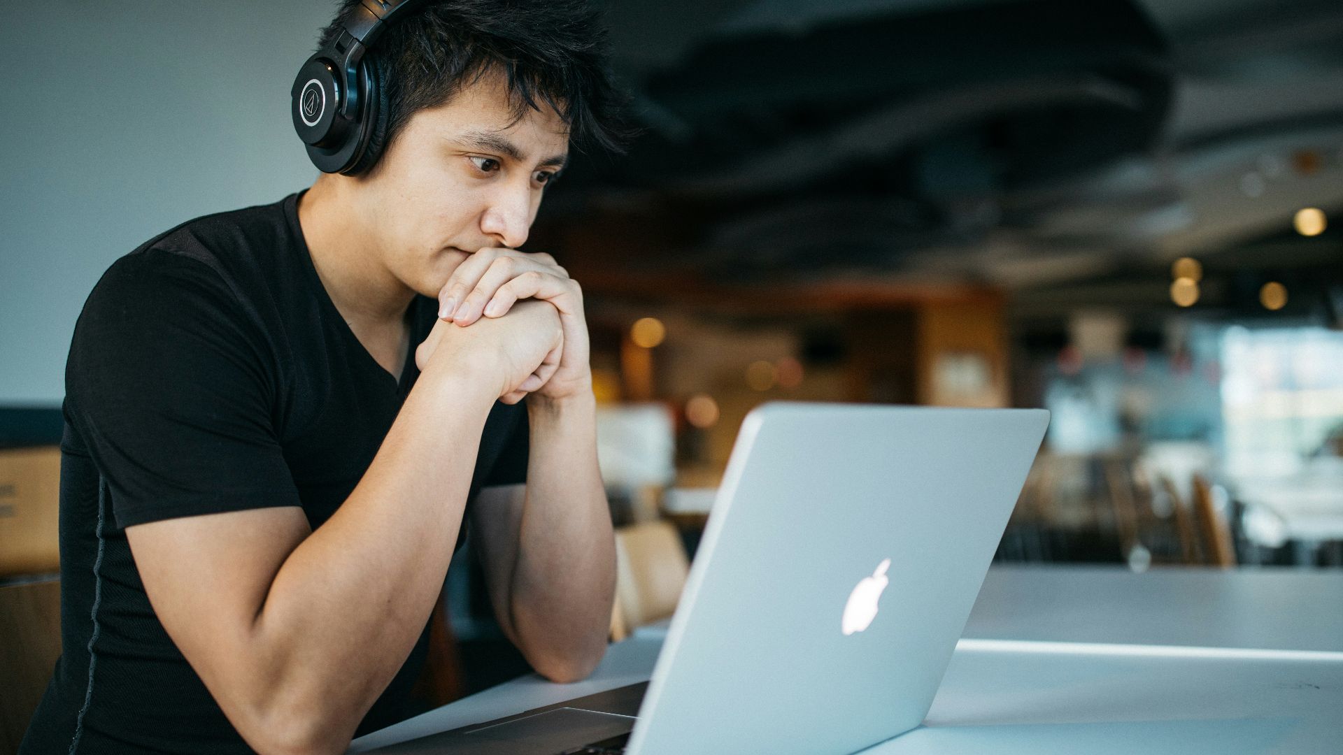 man wearing headphones while sitting on chair in front of MacBook