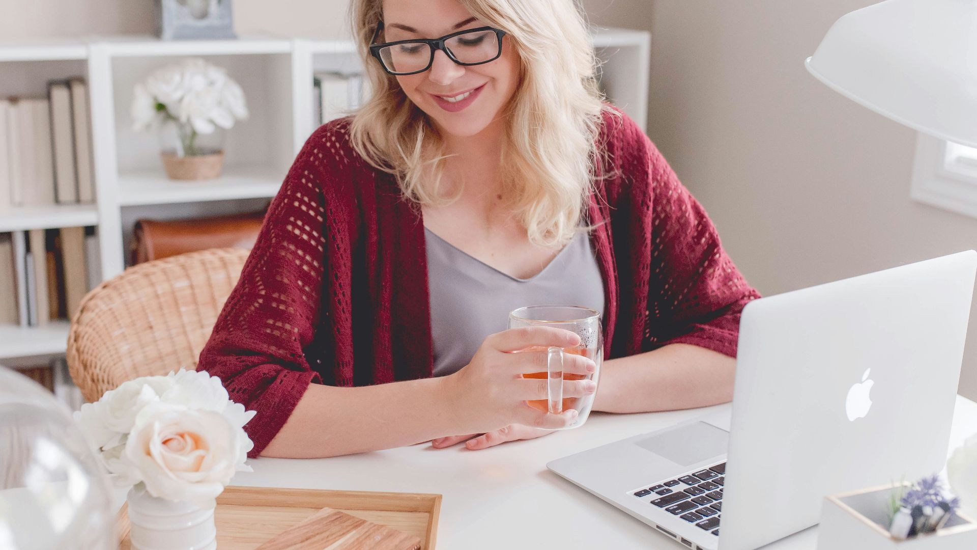 woman smiling holding glass mug sitting beside table with MacBook