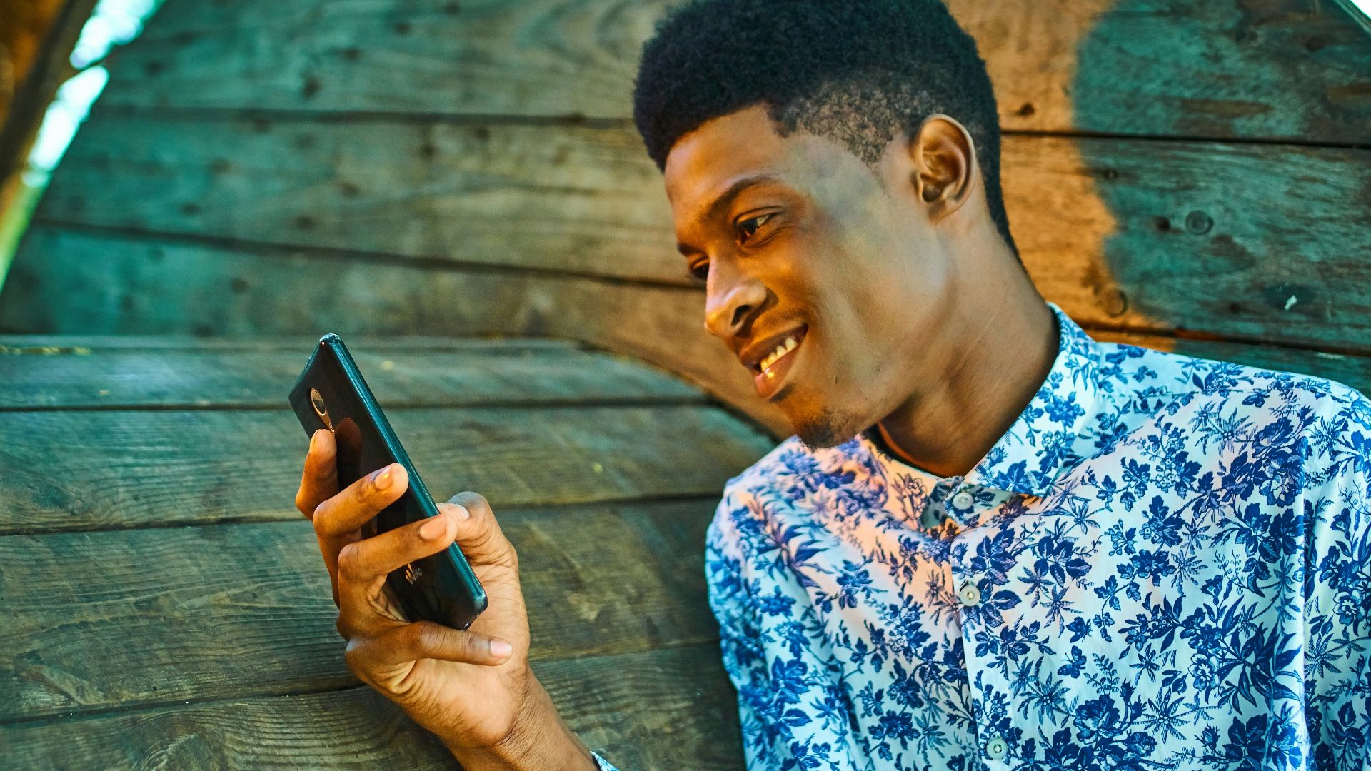 man in blue and white floral button up shirt holding black smartphone