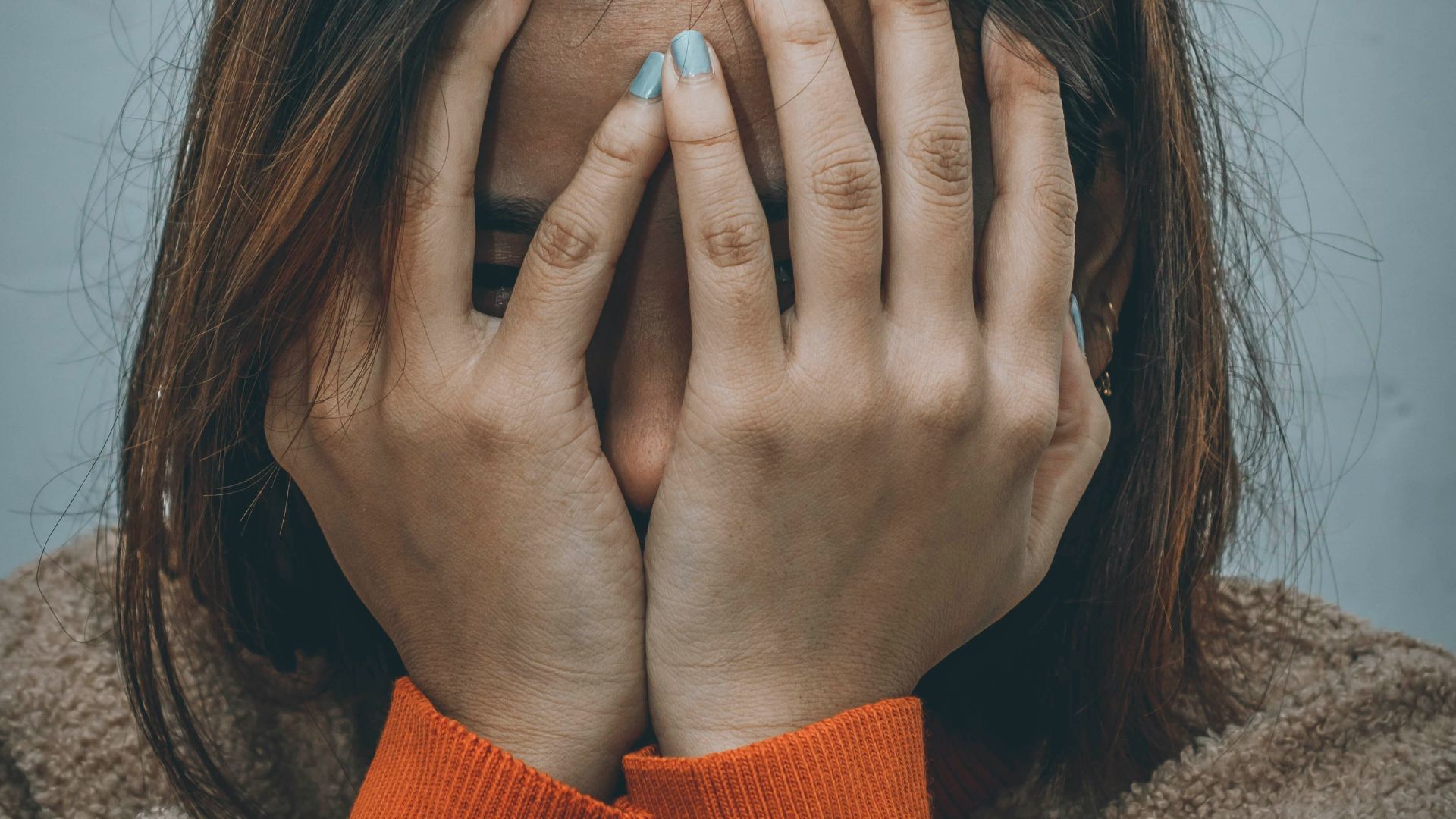 woman in brown sweater covering her face with her hand