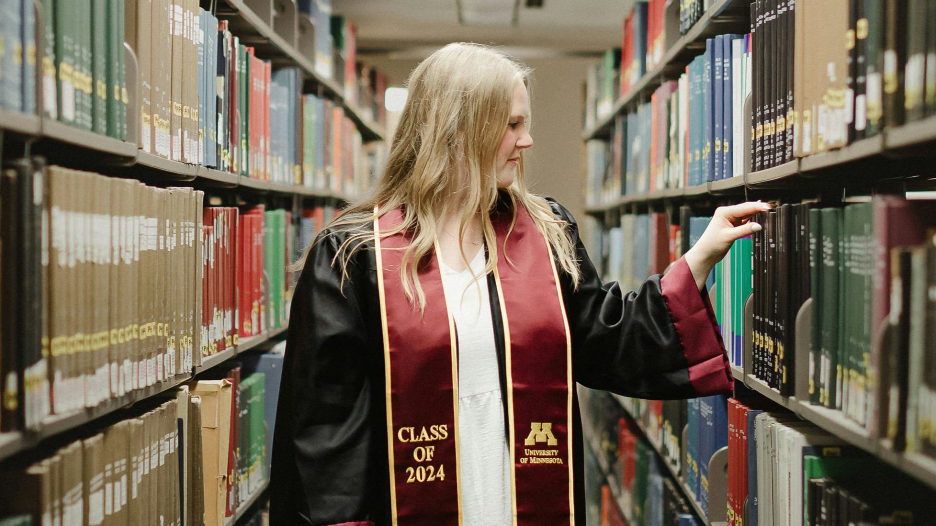 a woman in a graduation gown is walking through a library