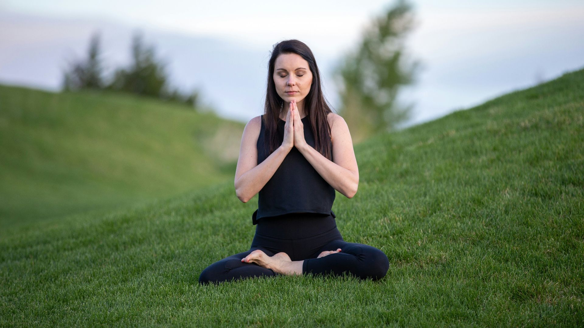 woman in black tank top and black pants sitting on green grass field during daytime