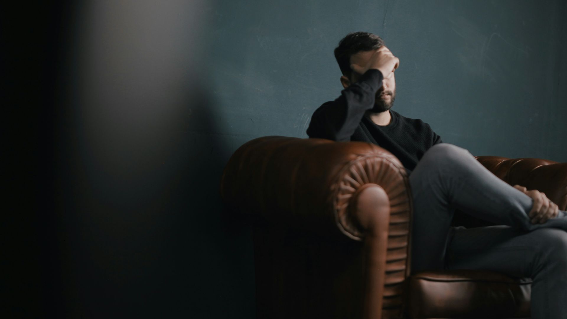 a man holds his head while sitting on a sofa