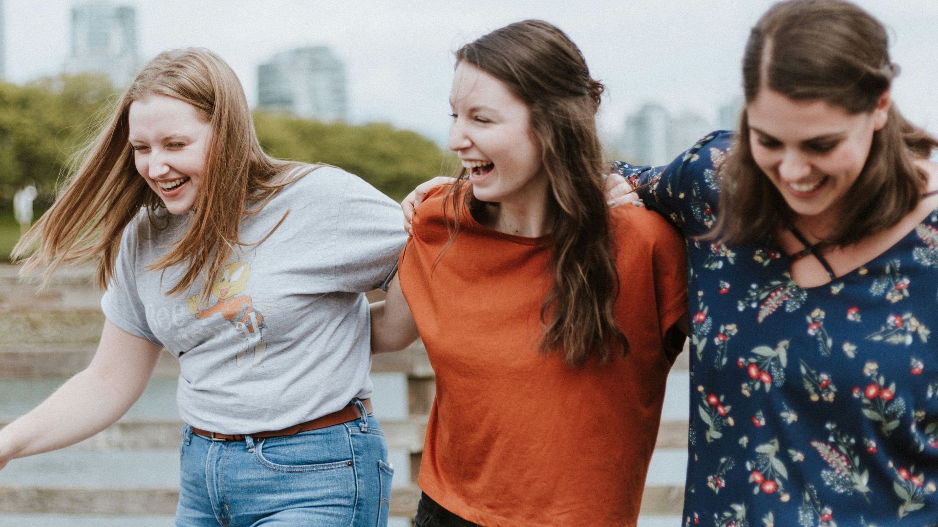 three women walking on brown wooden dock near high rise building during daytime