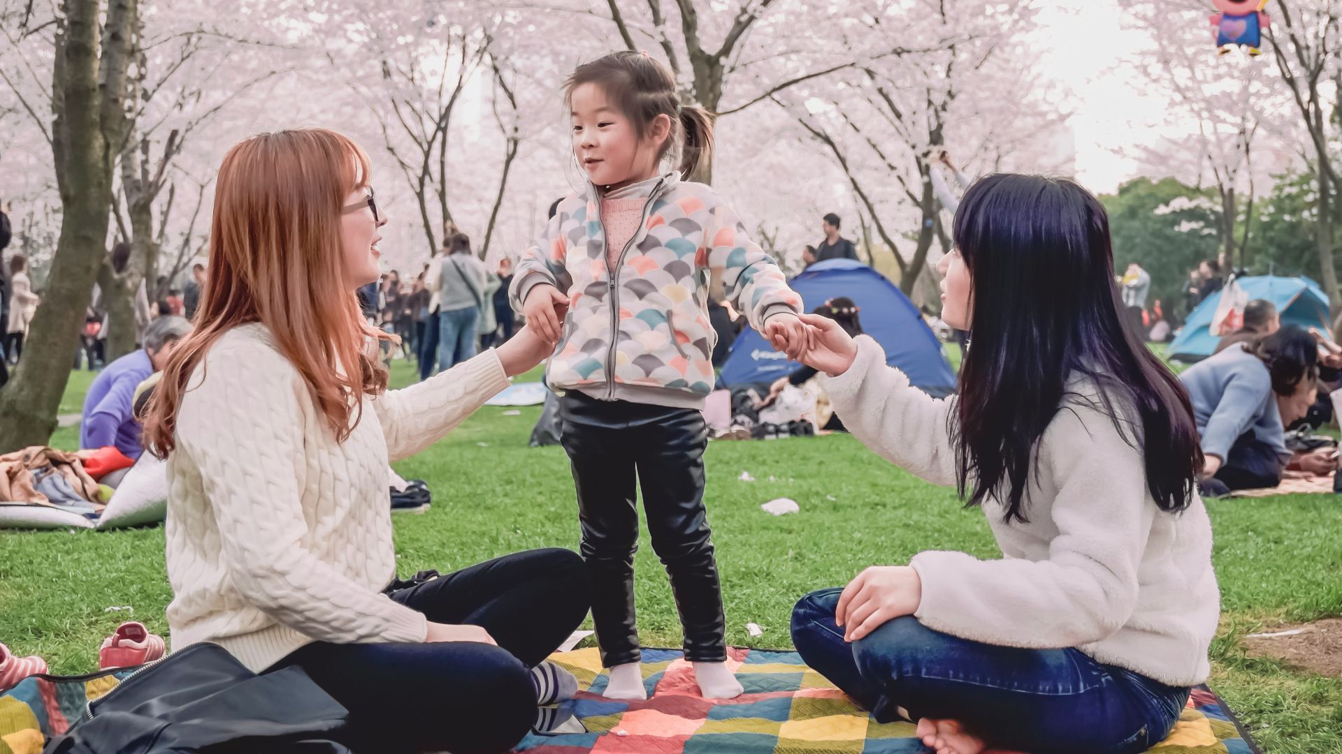 a group of women sitting on top of a blanket in a park
