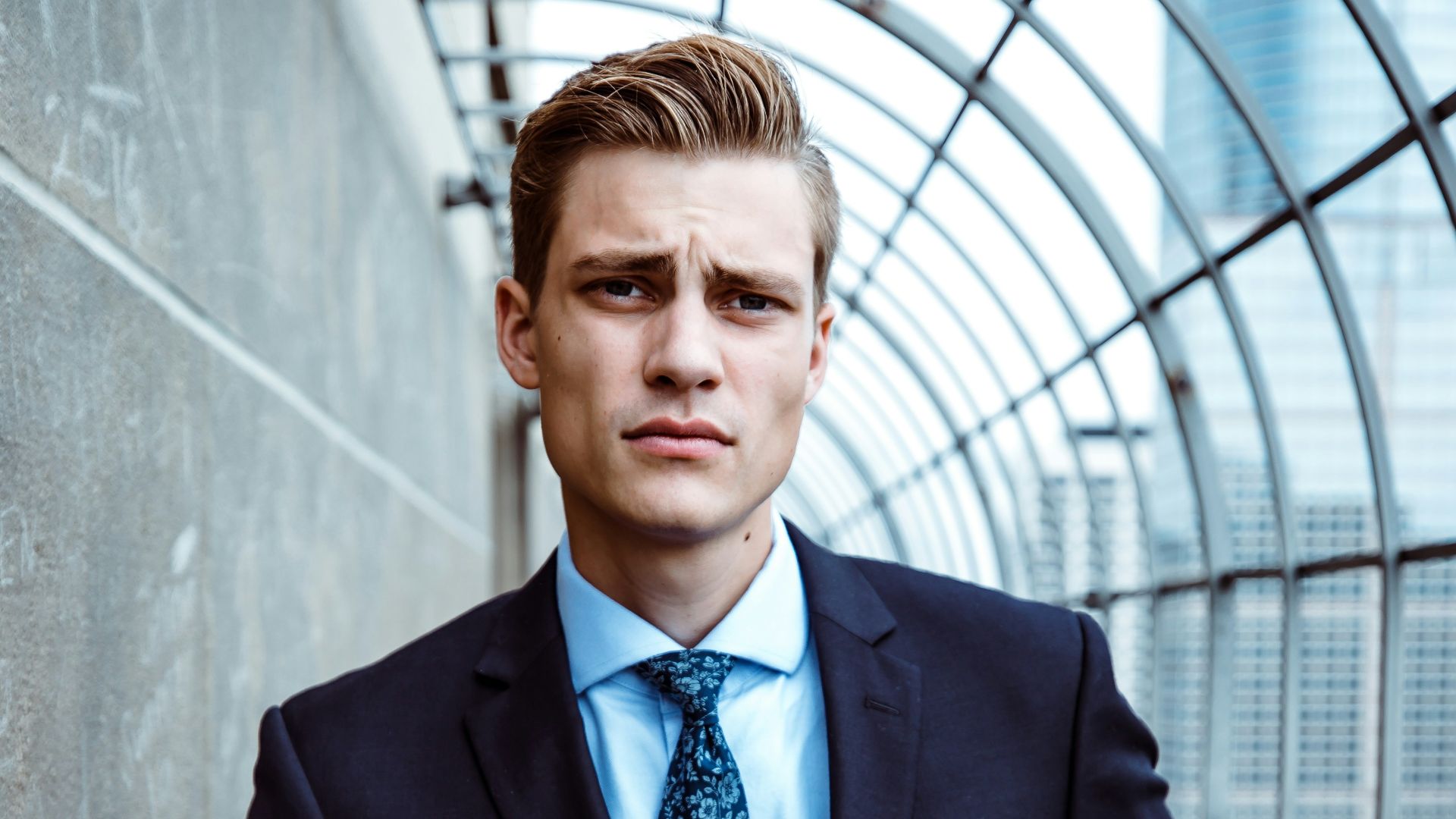 man wearing black and teal dress suit standing near gray wall