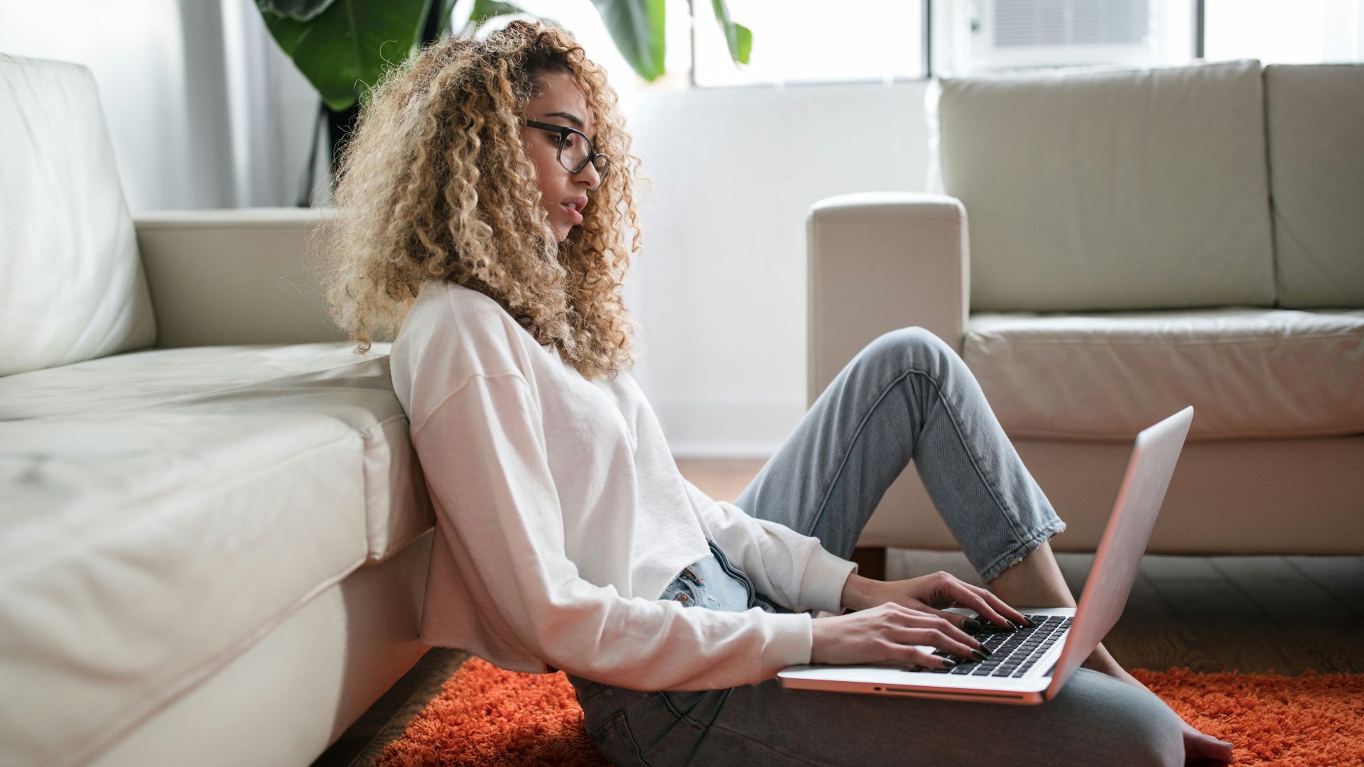 woman sitting on floor and leaning on couch using laptop