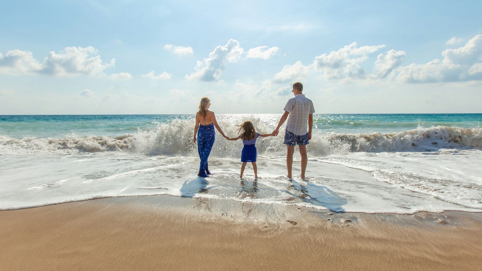 man, woman and child holding hands on seashore