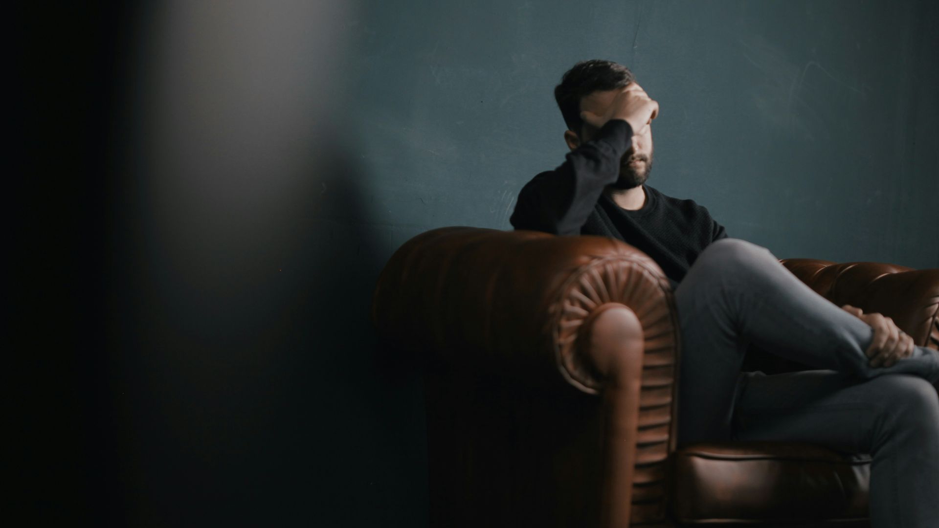 a man holds his head while sitting on a sofa