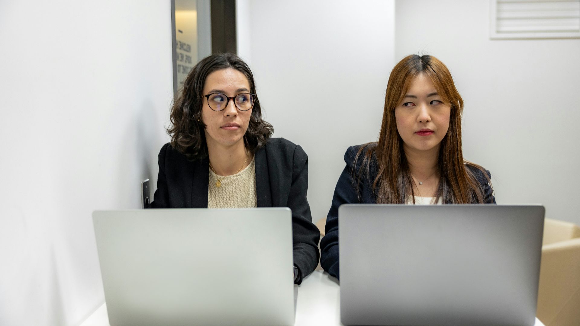two women sitting at a table with laptops
