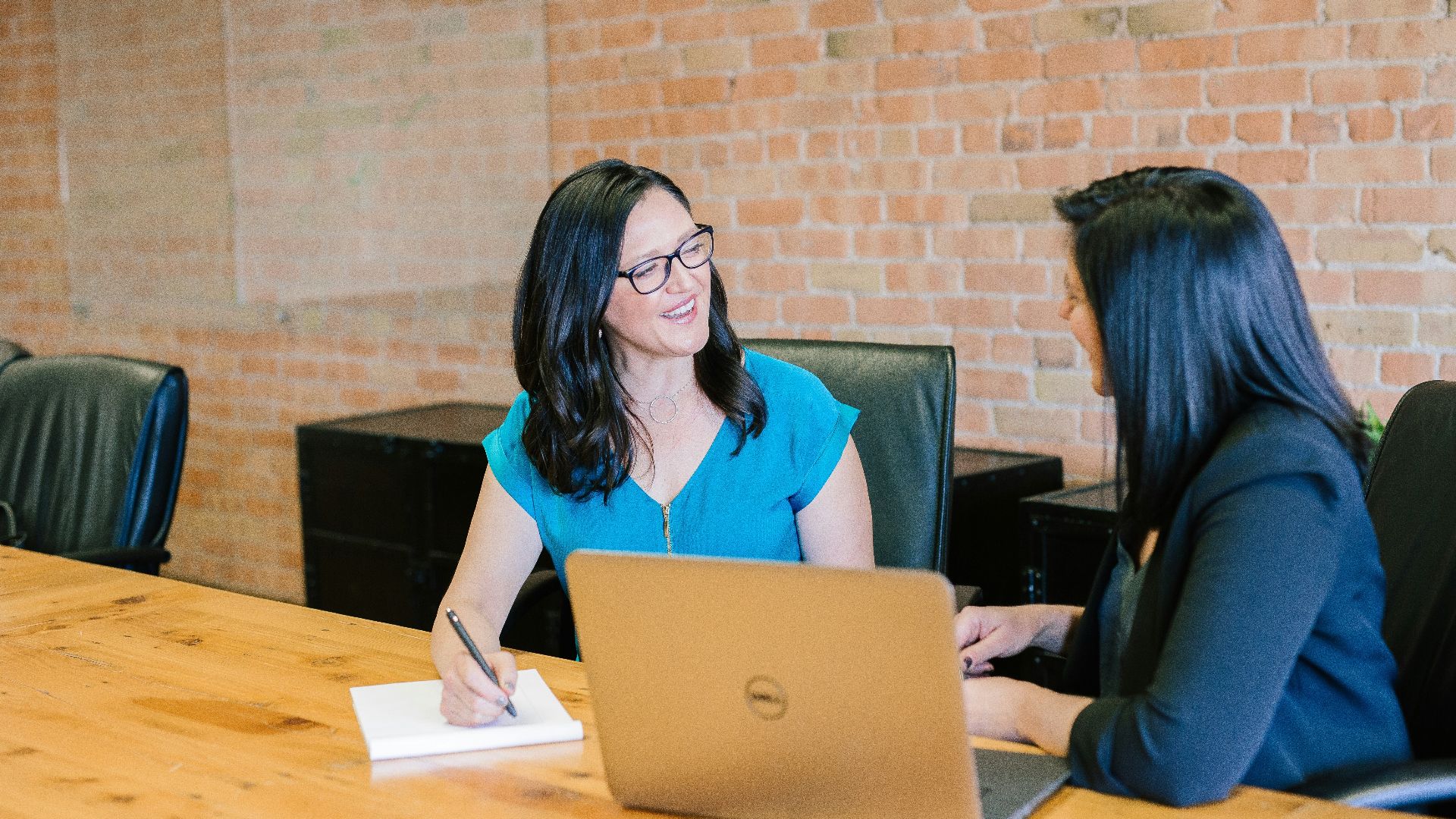 woman in teal t-shirt sitting beside woman in suit jacket