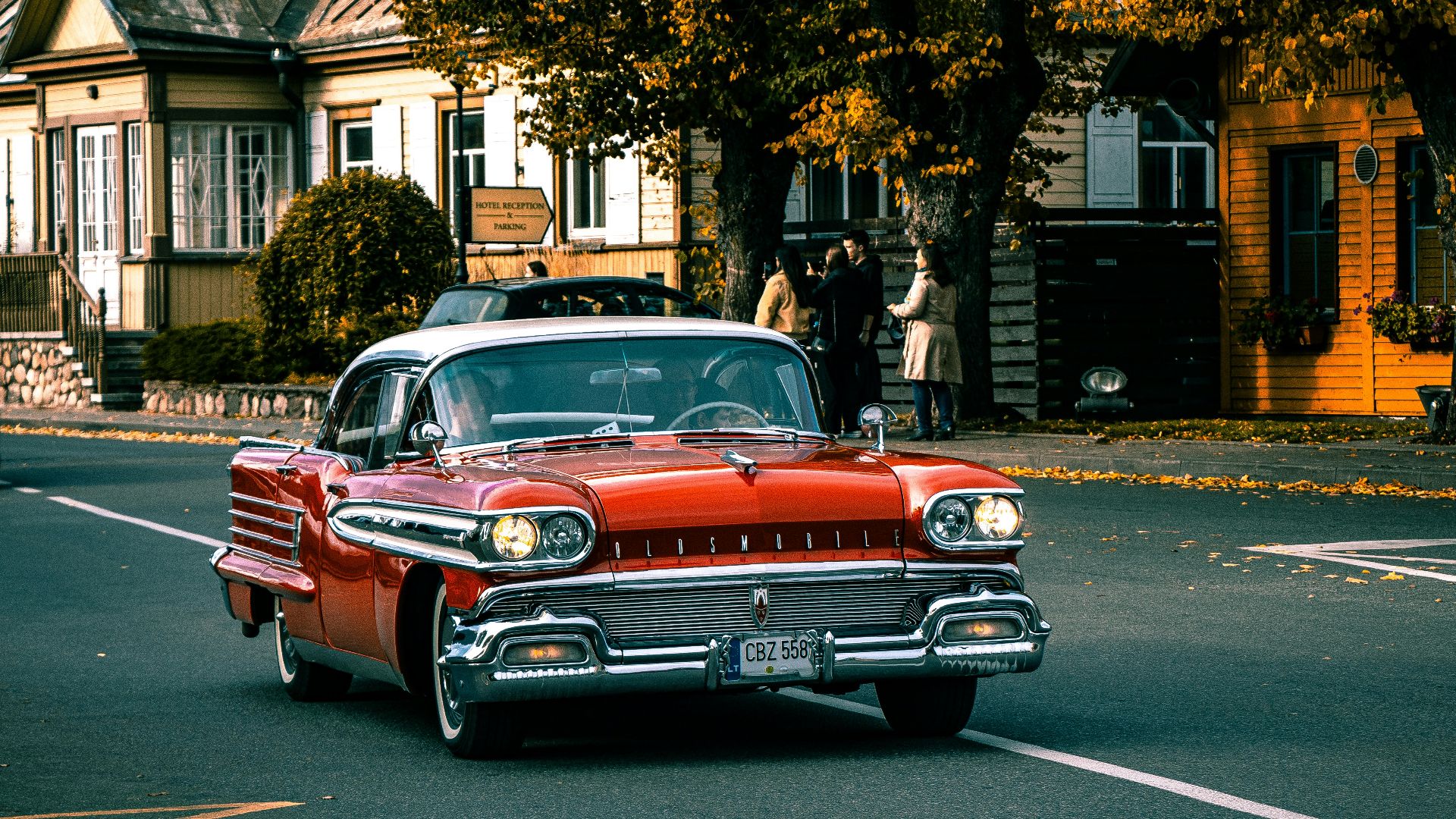 a red car driving down a street next to a house