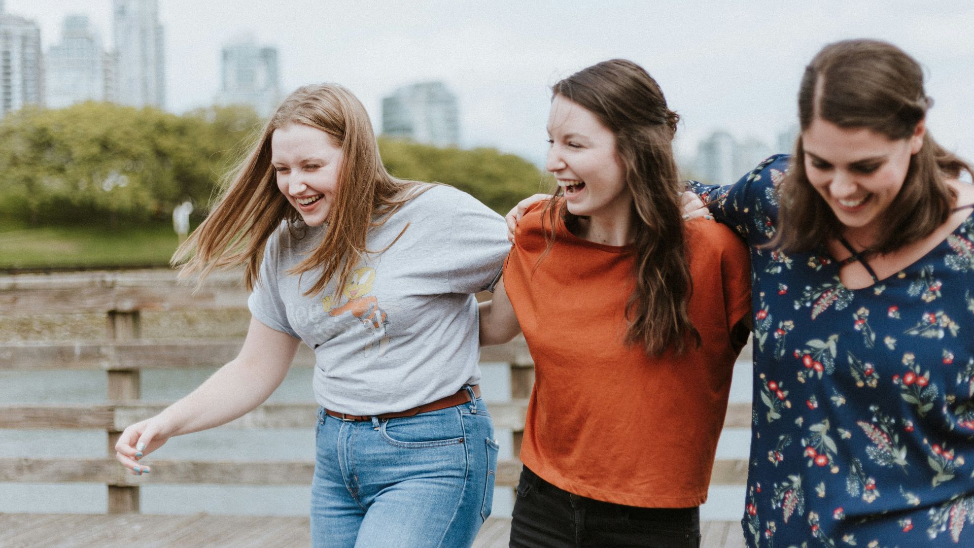 three women walking on brown wooden dock near high rise building during daytime