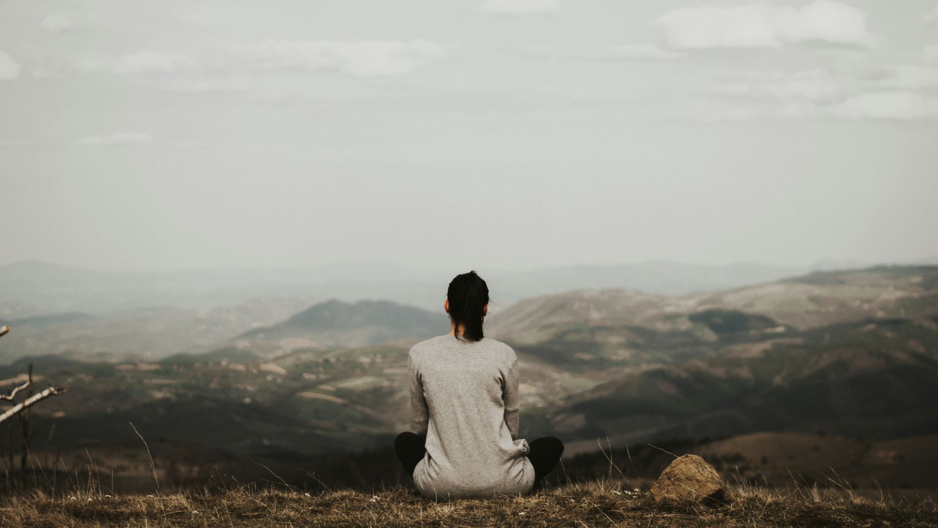 woman sitting on cliff overlooking mountains during daytime
