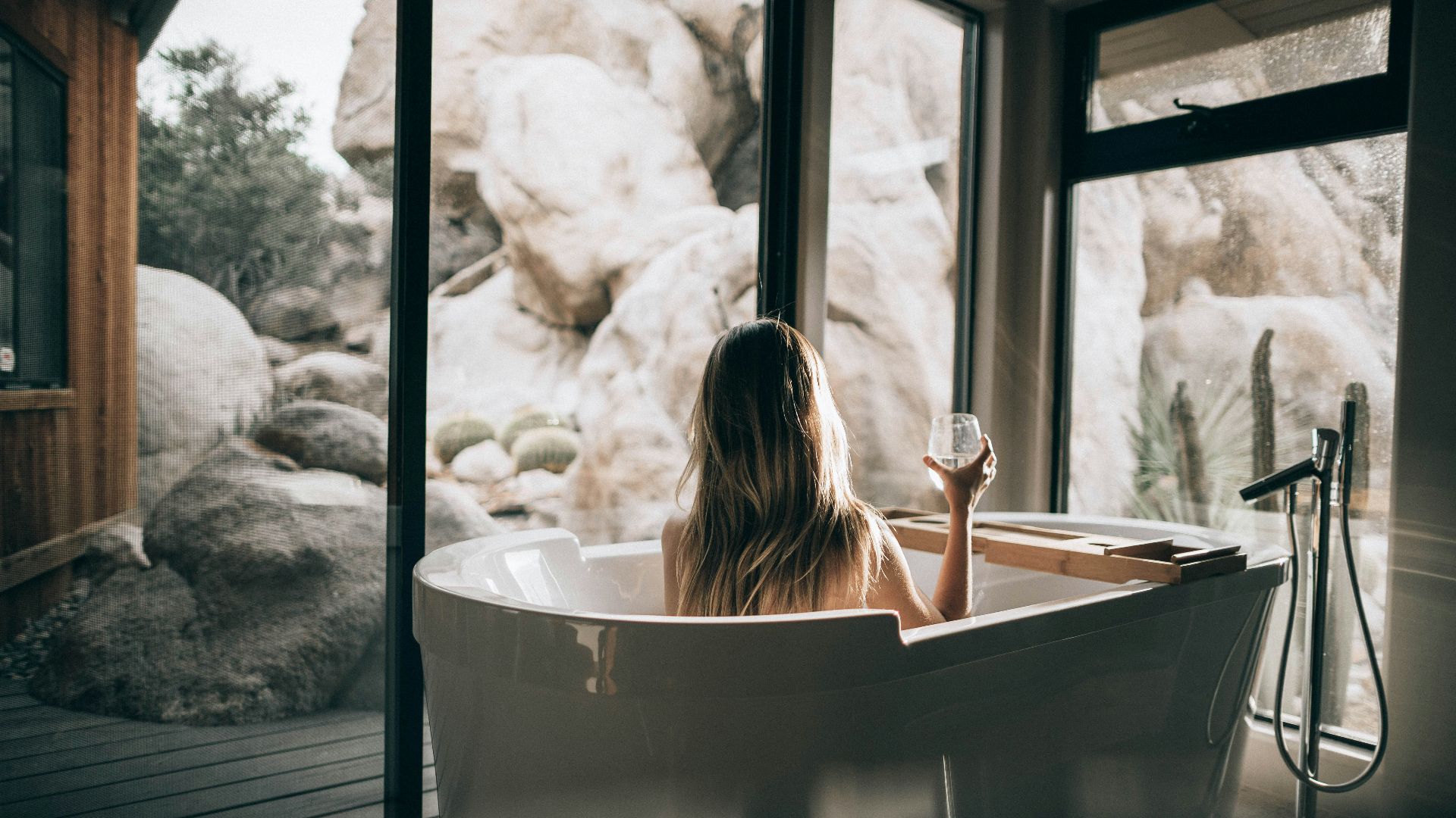 woman in white bathtub holding clear drinking glass