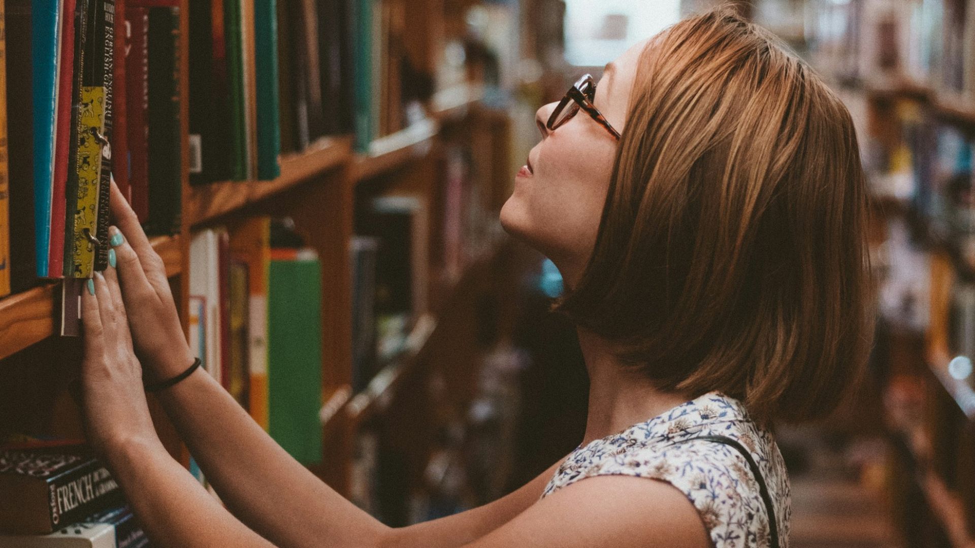 woman standing between library book shelves