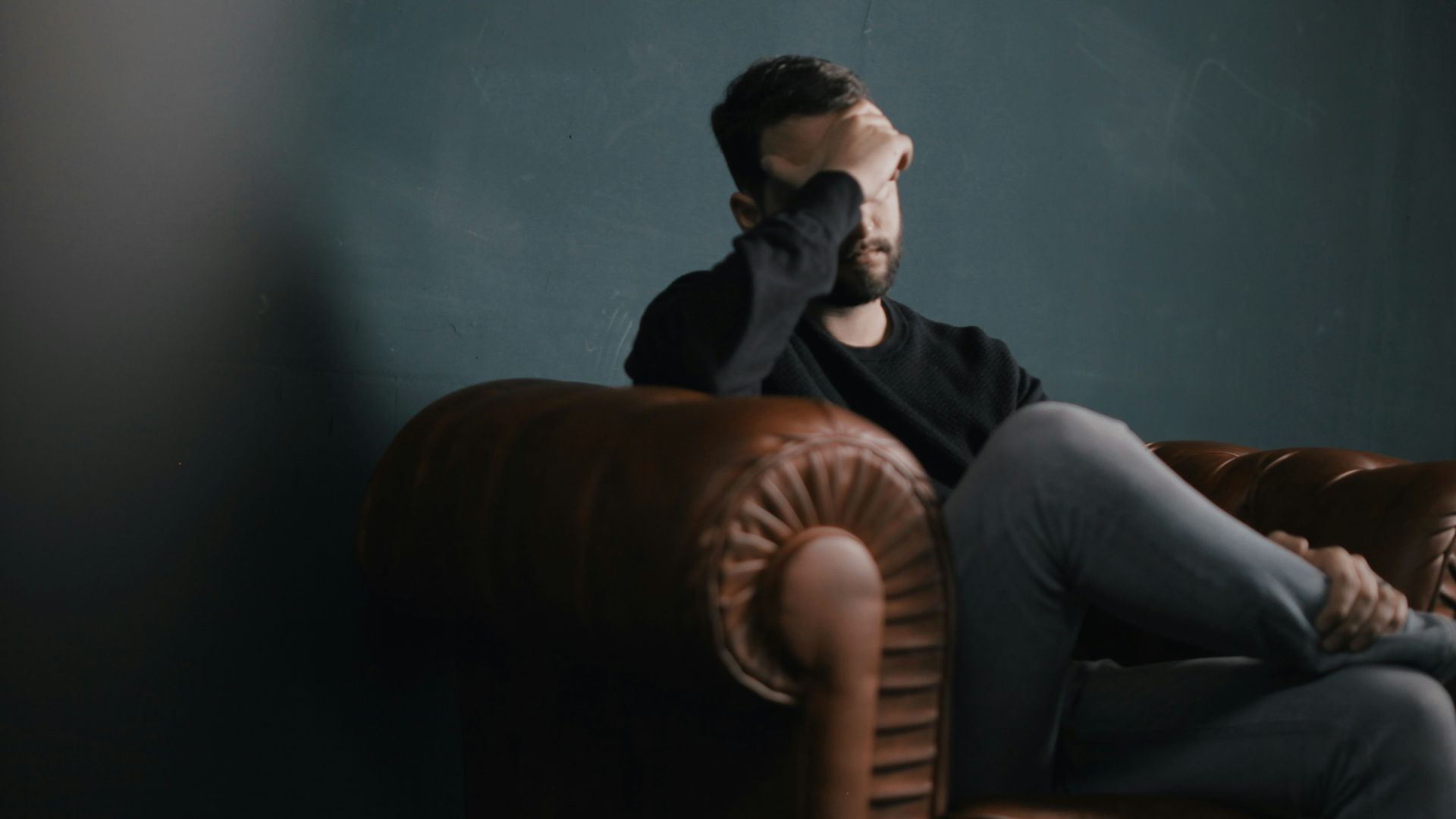 a man holds his head while sitting on a sofa