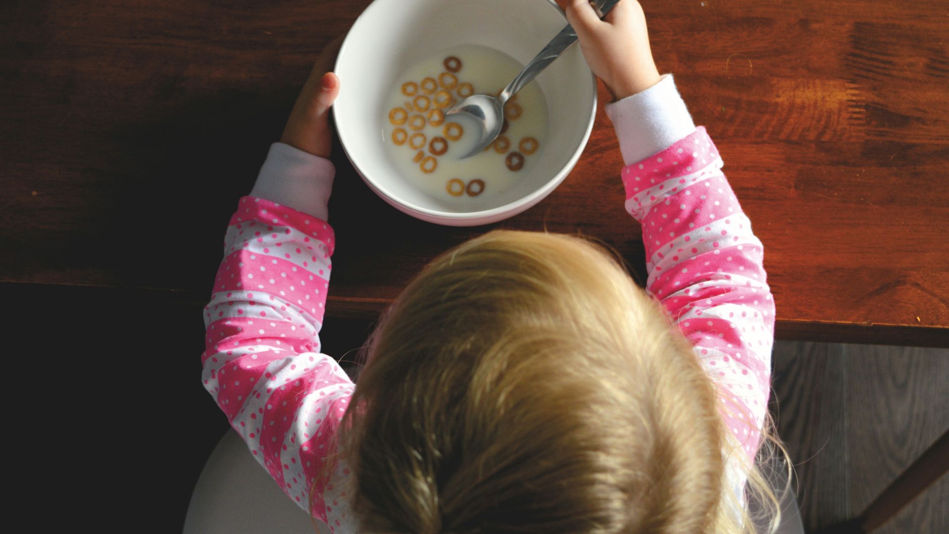 girl eating cereal in white ceramic bowl on table