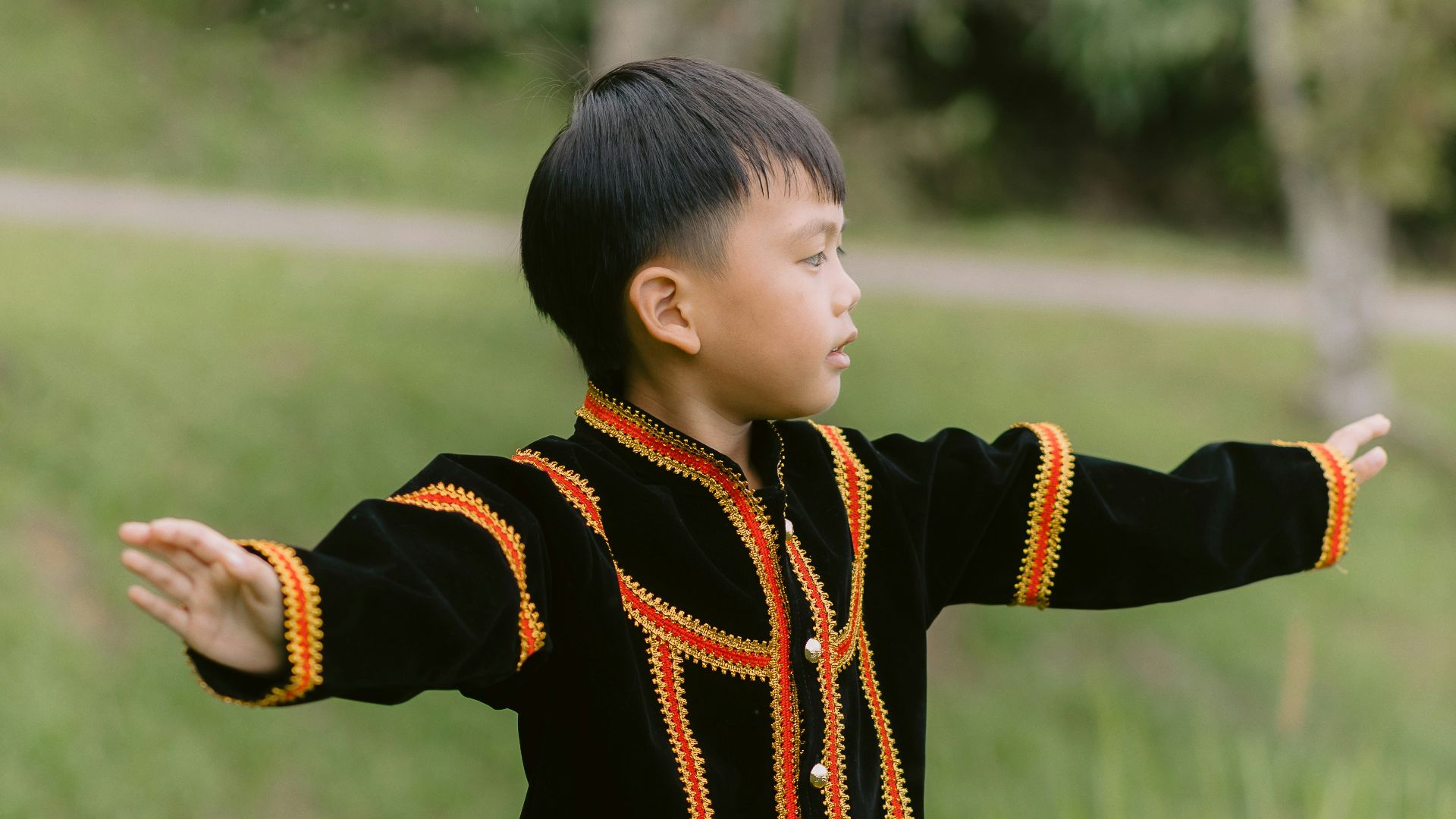 A boy poses in traditional attire outdoors.