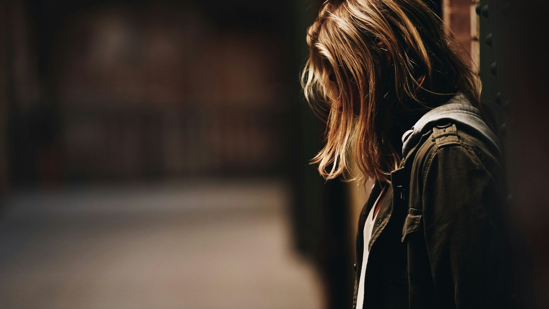 woman leaning against a wall in dim hallway