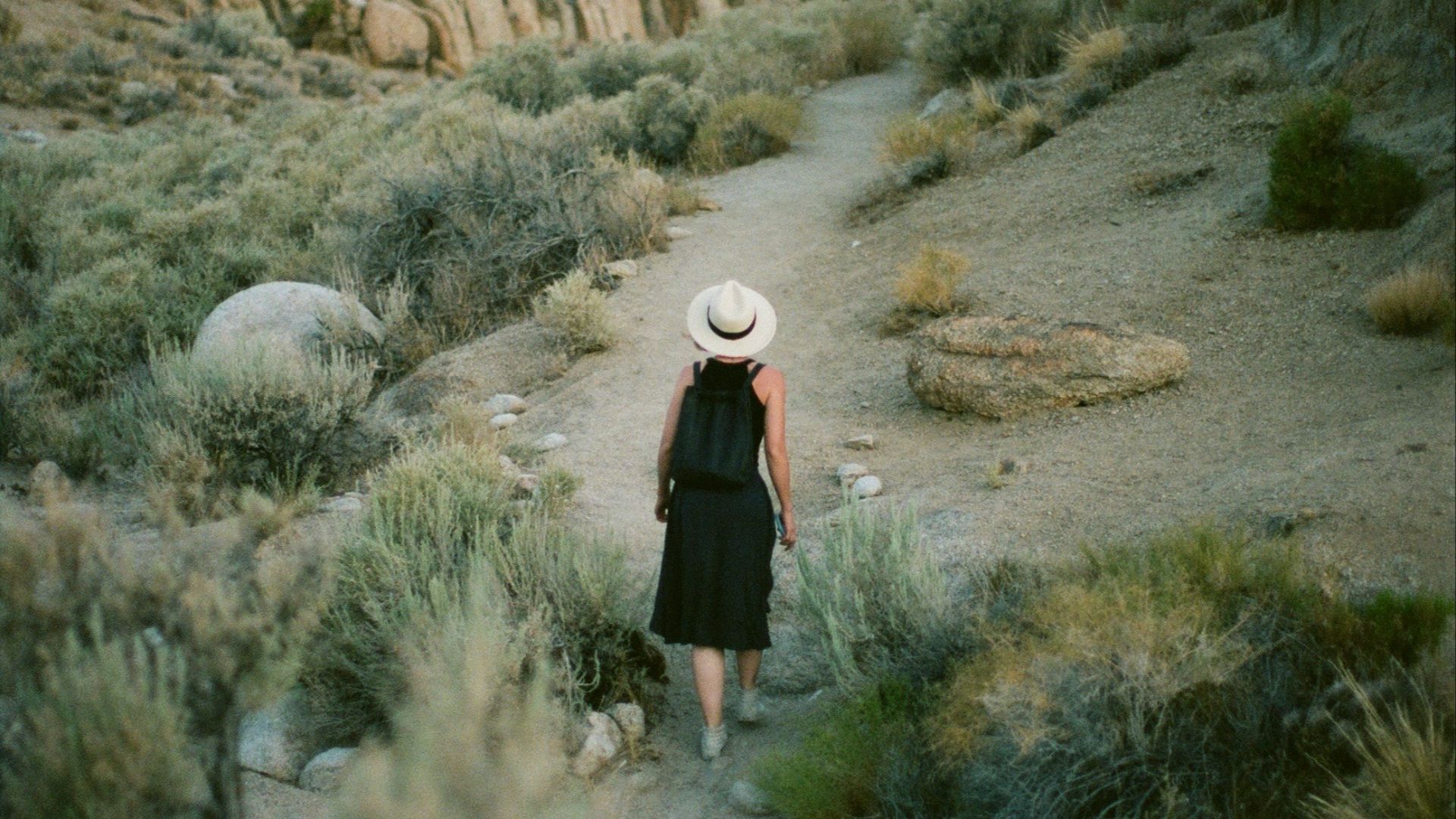woman in black dress walking on dirt road during daytime