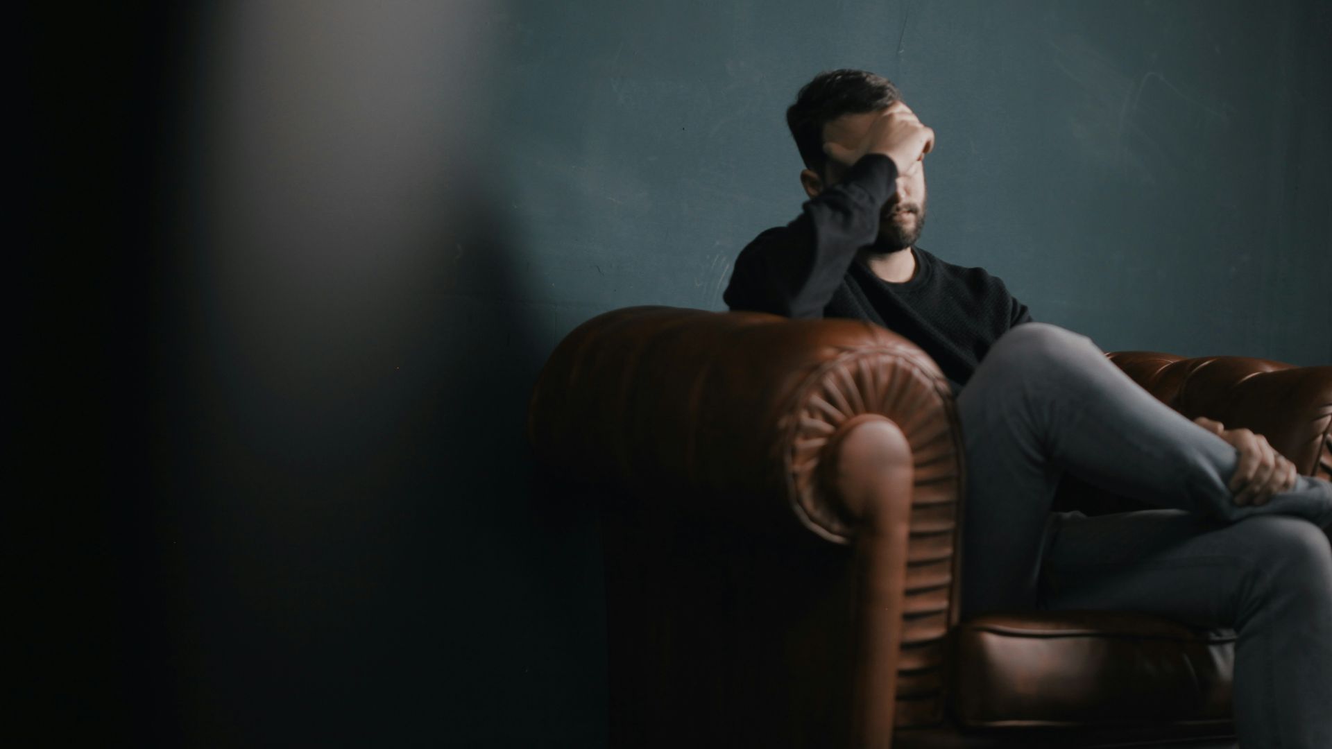 a man holds his head while sitting on a sofa