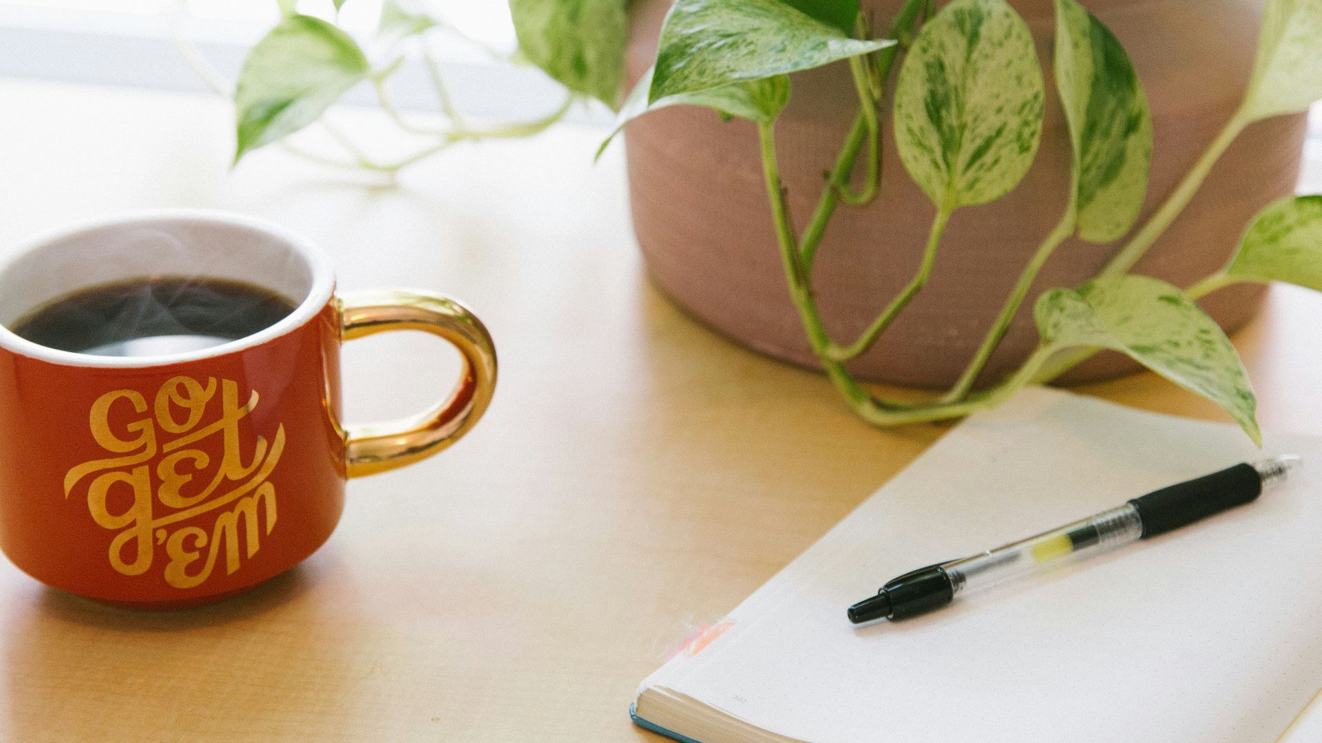 black retractable pen on opened book beside red and white go get'em-printed coffee cup
