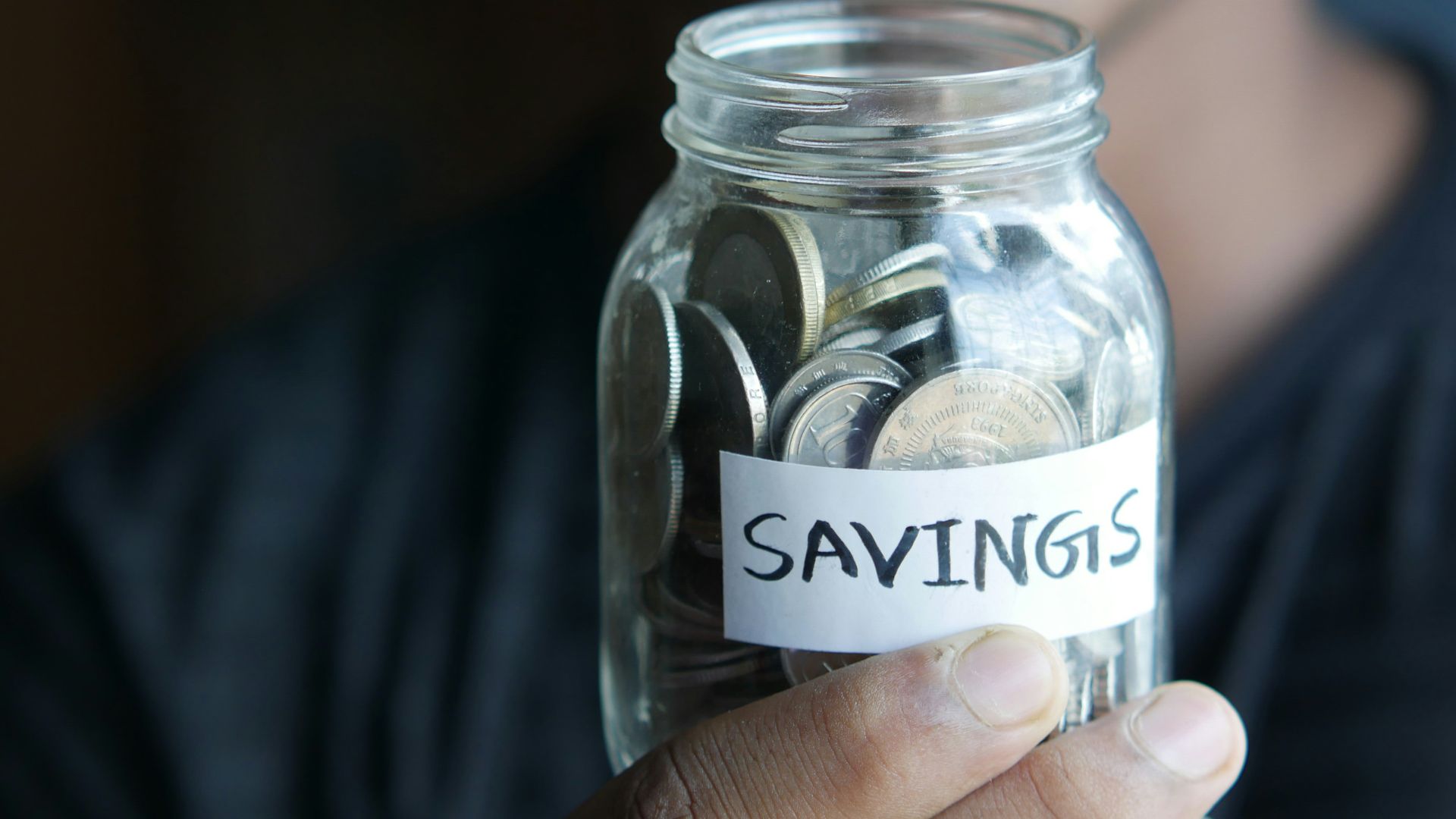 a man holding a jar with a savings label on it