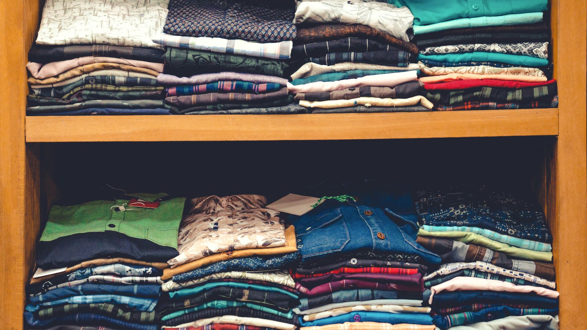 a wooden shelf filled with lots of folded shirts