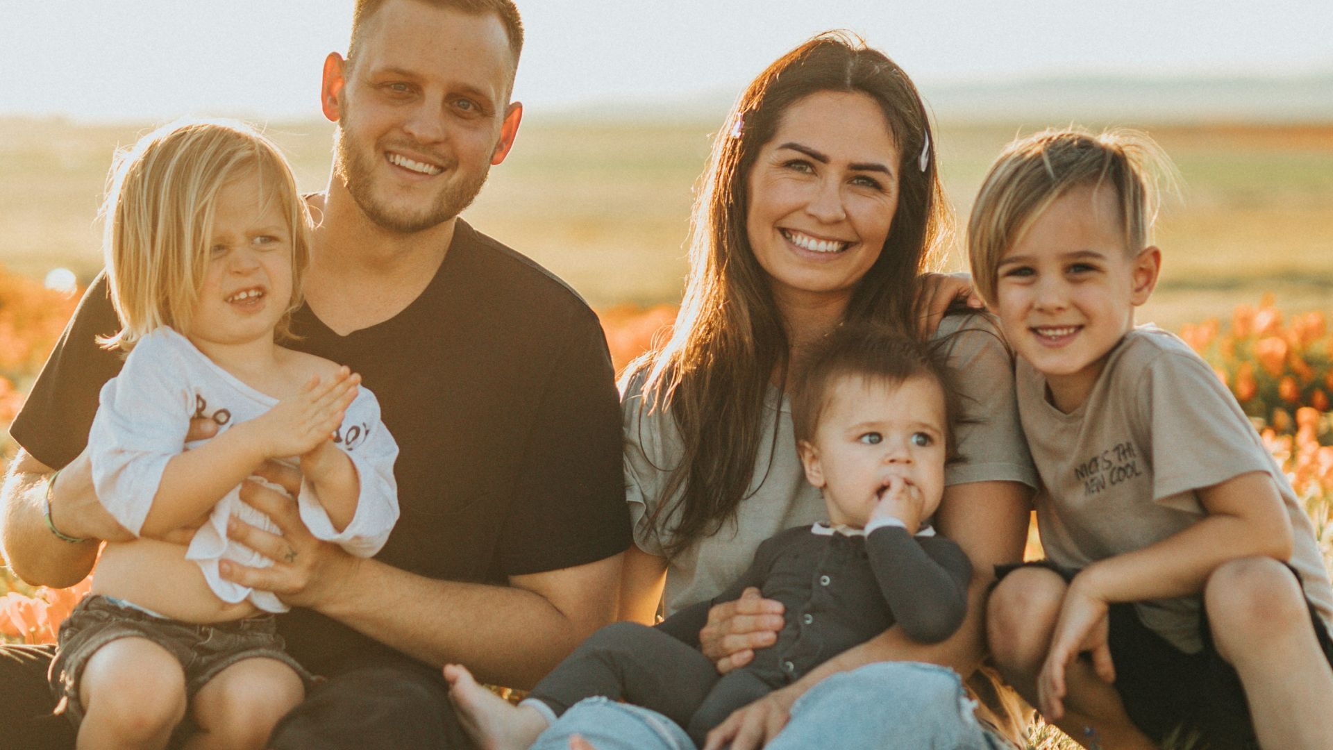 3 women and 2 men sitting on green grass field during daytime