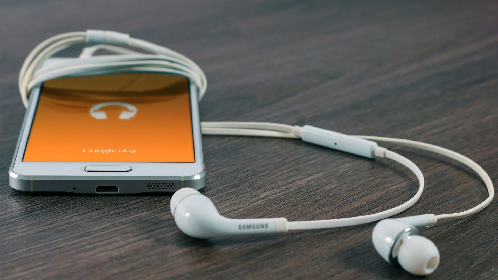 white Samsung Android smartphone turned beside white earbuds on brown board