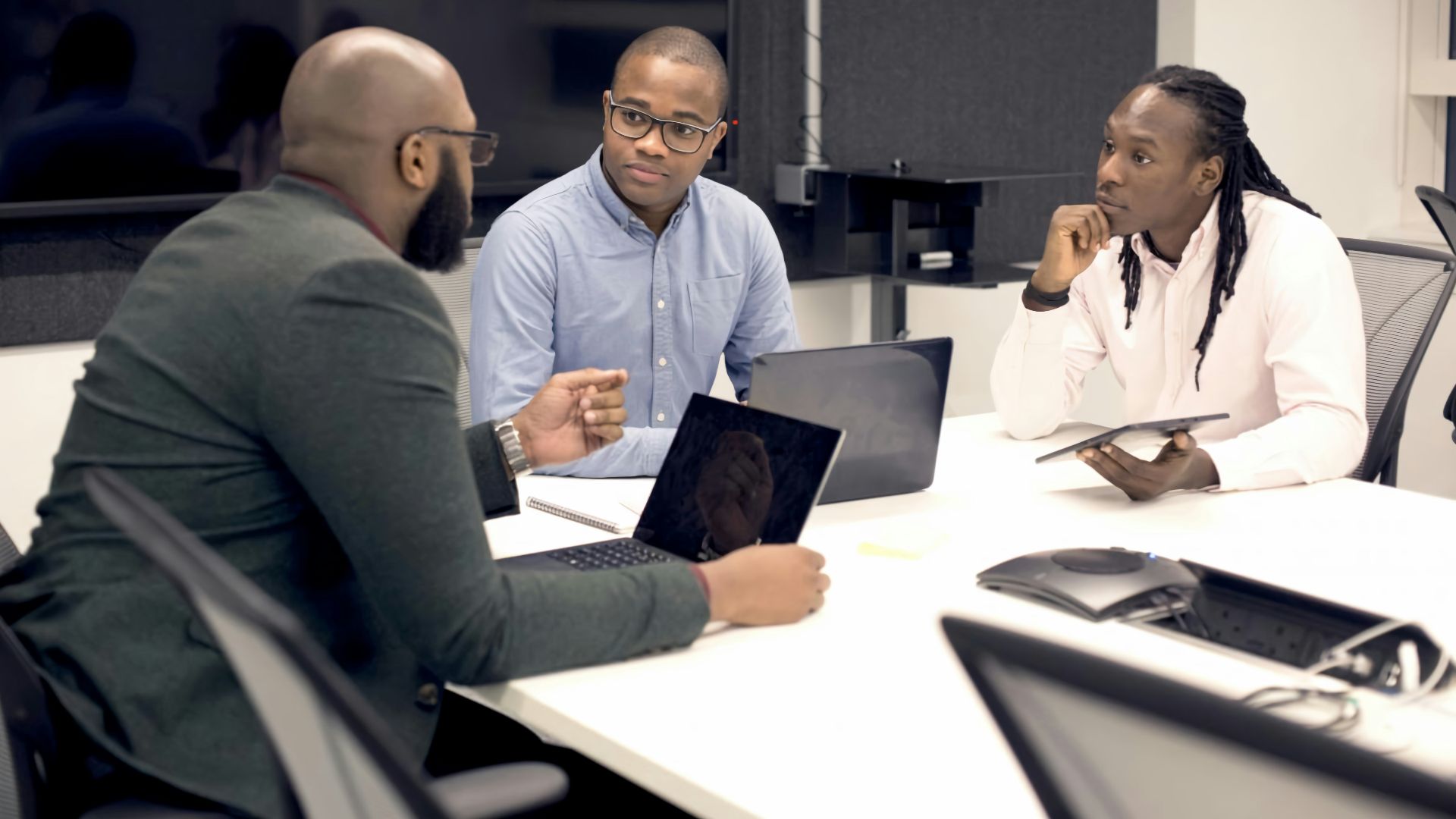 a group of people sitting around a table with laptops