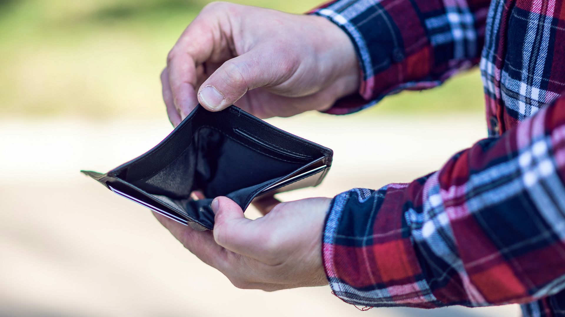 person in red blue and white plaid long sleeve shirt holding black leather bifold wallet