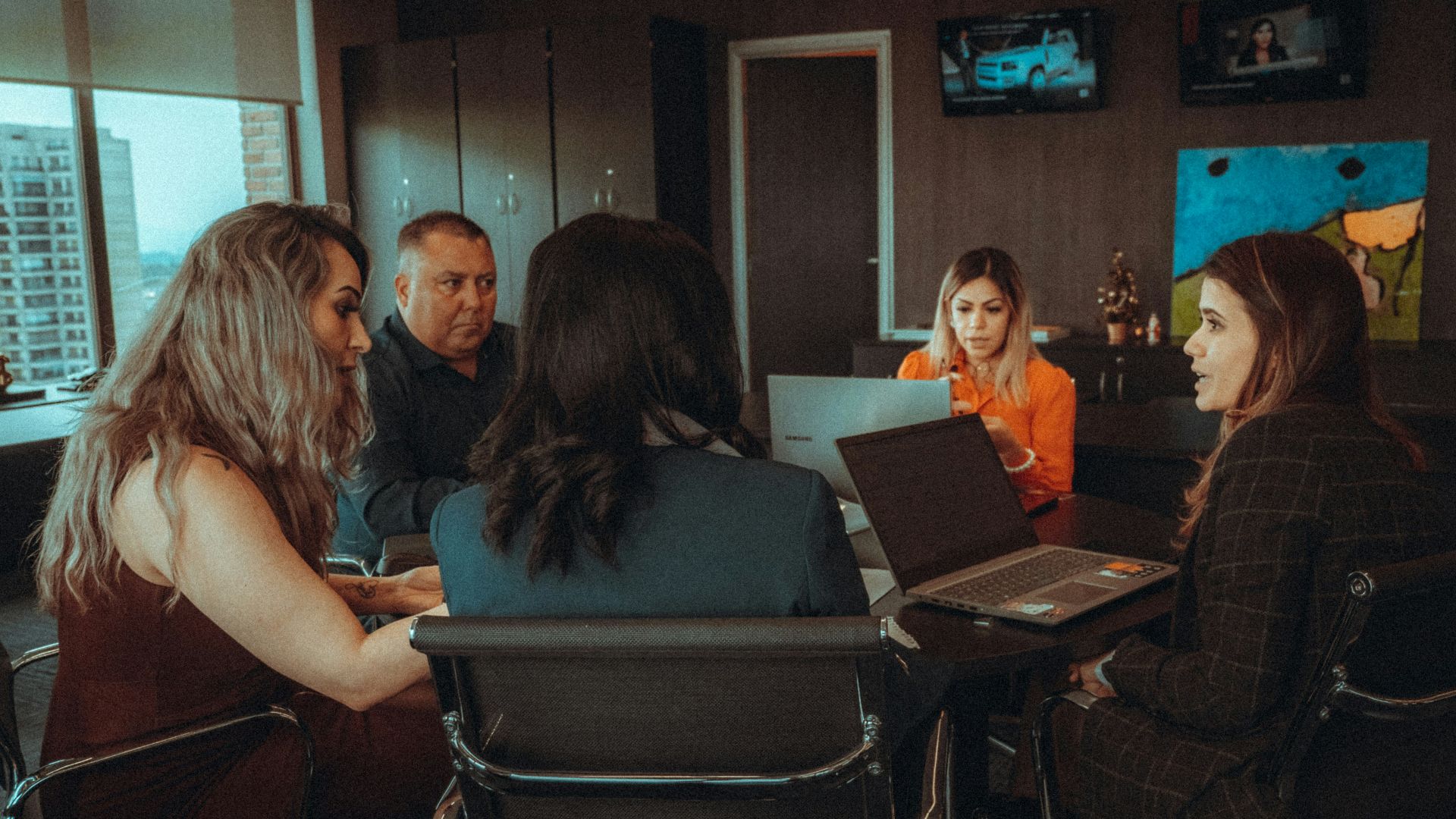 a group of people sitting around a table with laptops