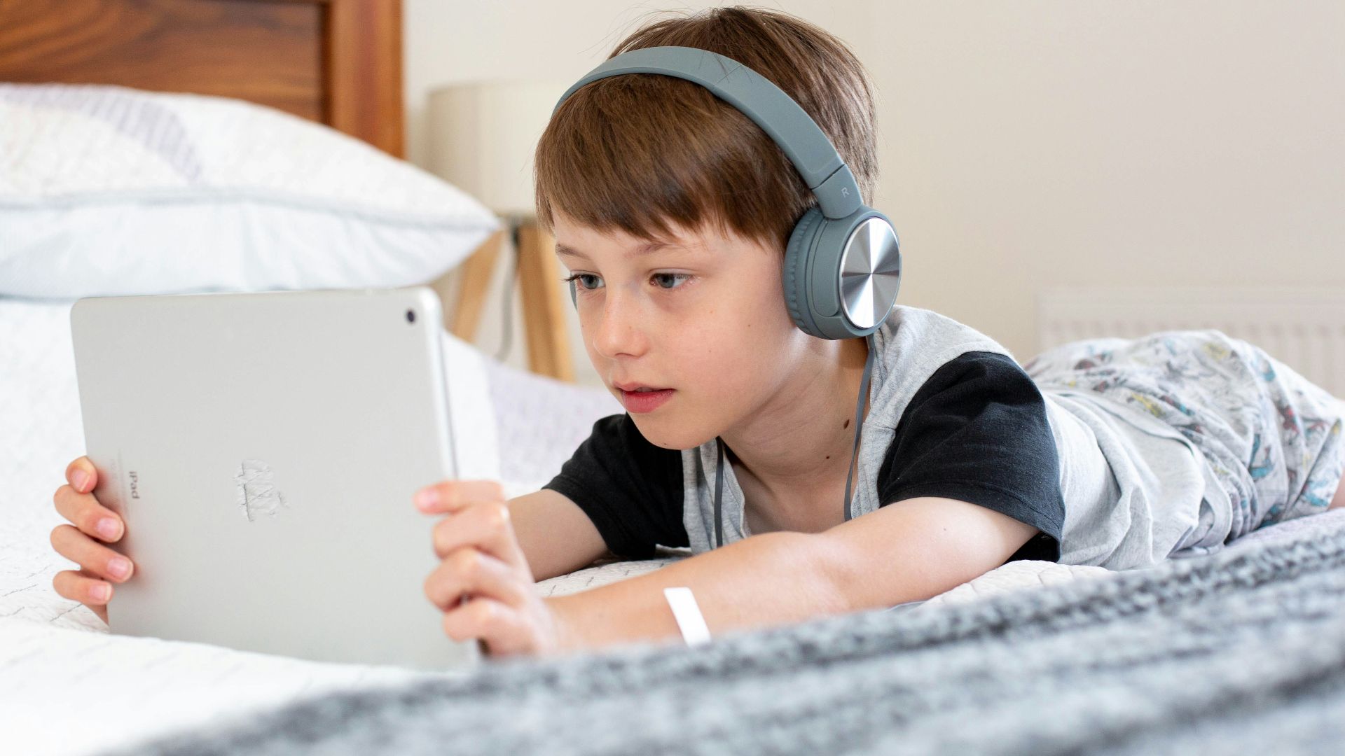 boy in blue shirt wearing headphones lying on bed