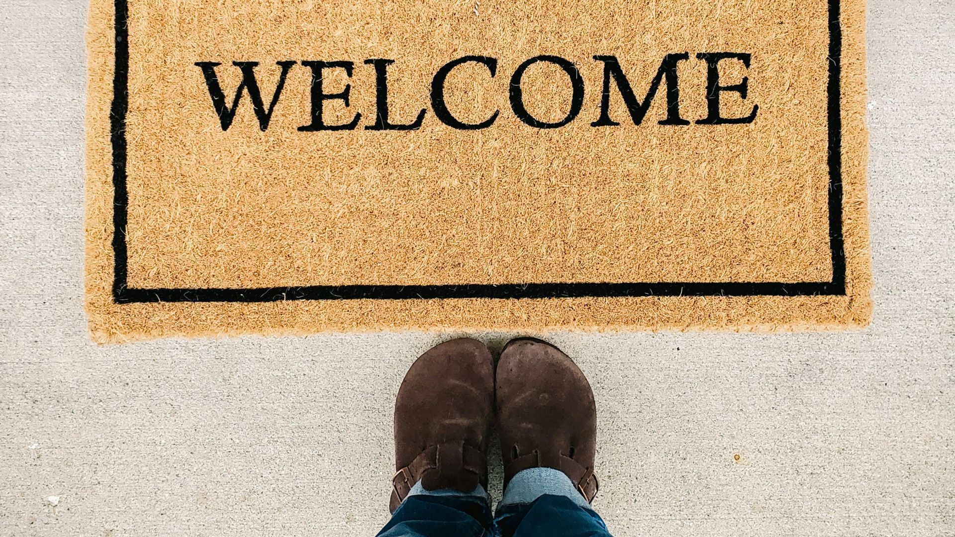 person in blue denim jeans standing on brown and black welcome area rug