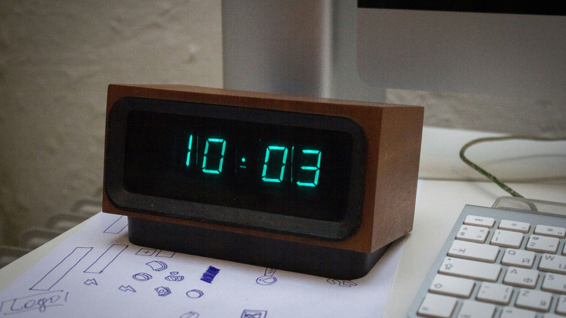 A digital clock sitting on top of a desk next to a keyboard