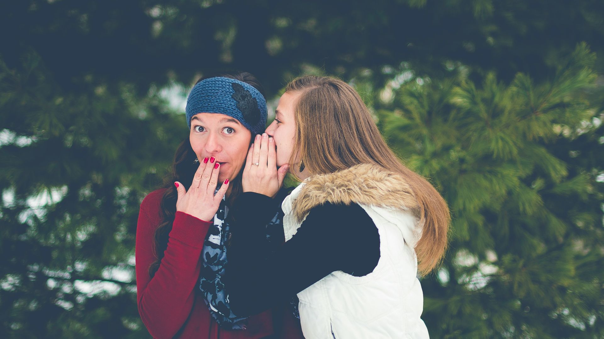 woman whispering on woman's ear while hands on lips