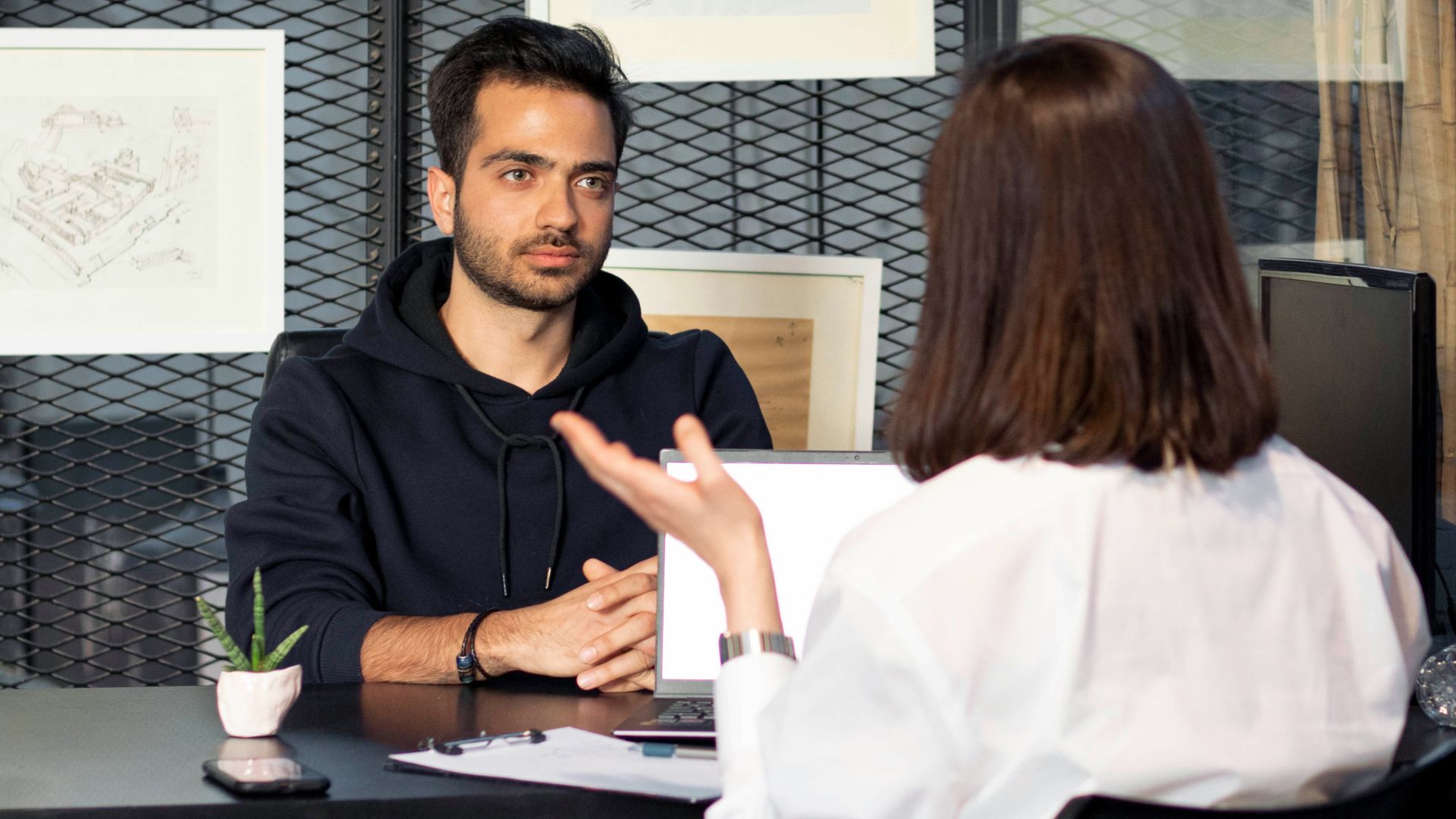 a man sitting at a desk talking to a woman