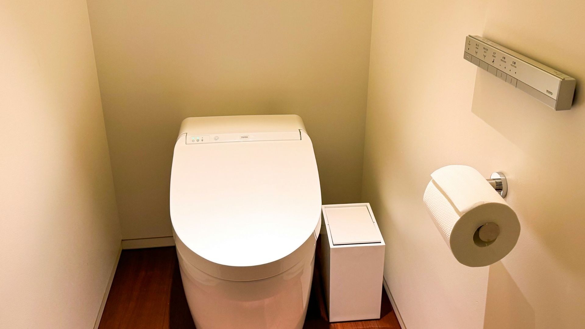 A white toilet sitting in a bathroom next to a roll of toilet paper