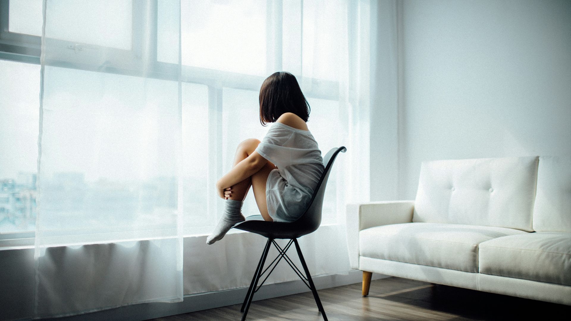 woman sitting on black chair in front of glass-panel window with white curtains