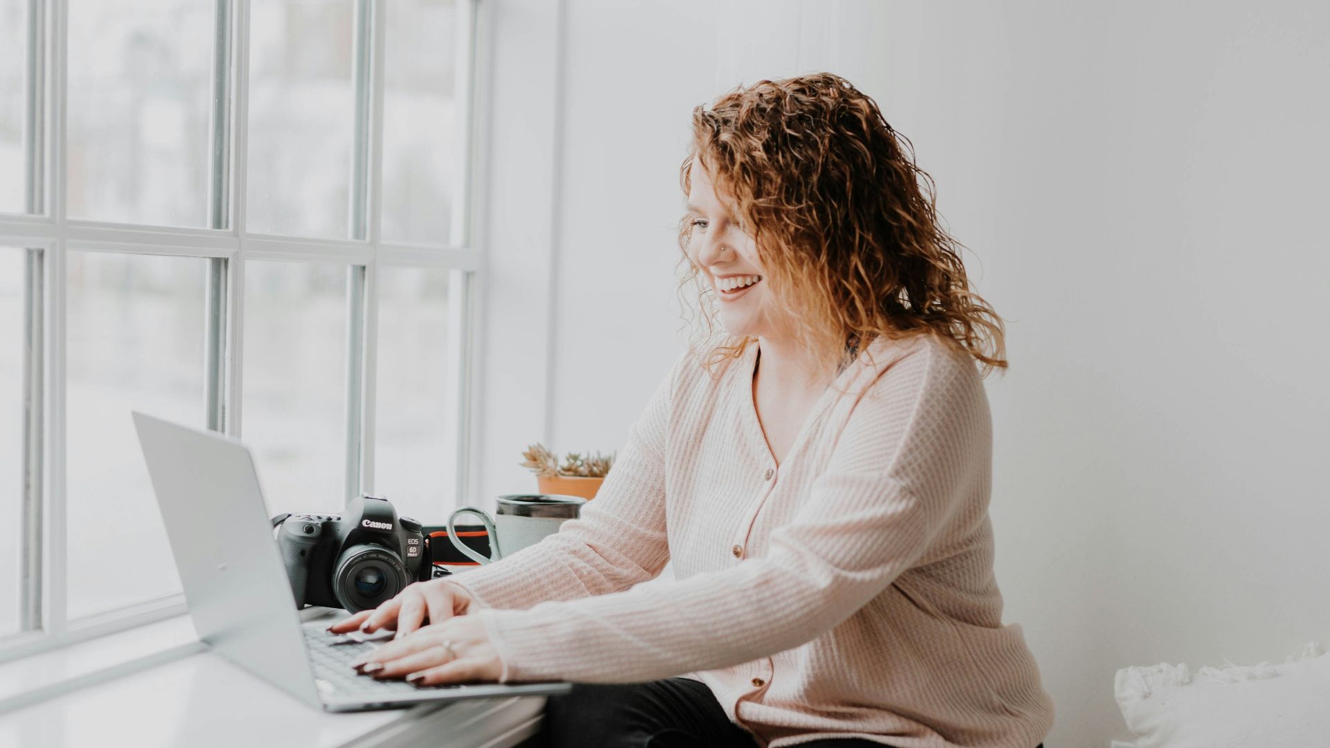woman in white long sleeve shirt and black pants sitting on bed using laptop computer