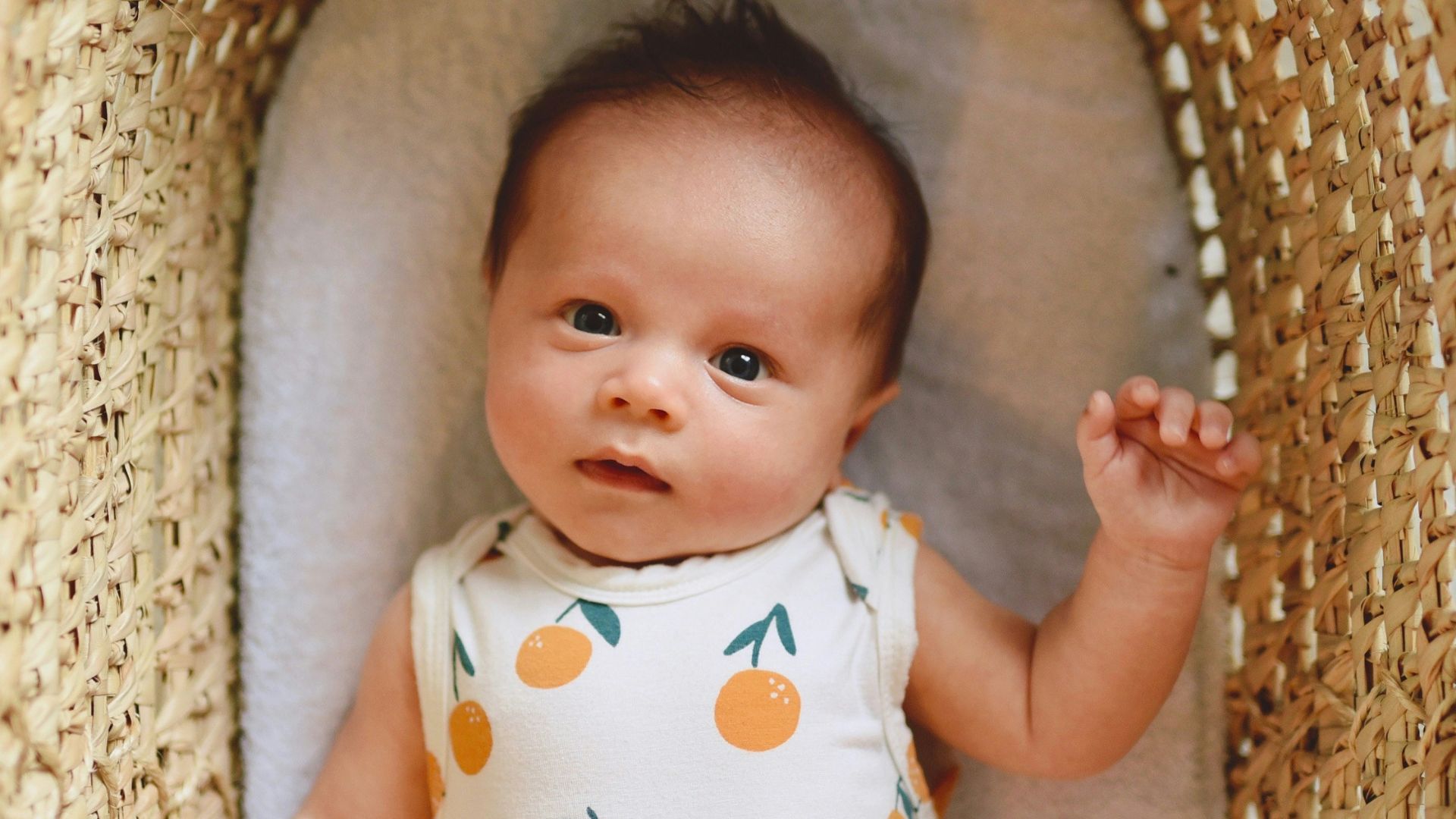 baby in white and green polka dot onesie lying on brown wicker basket