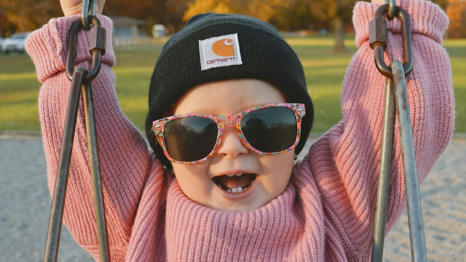 a little girl wearing sunglasses and a hat on a swing