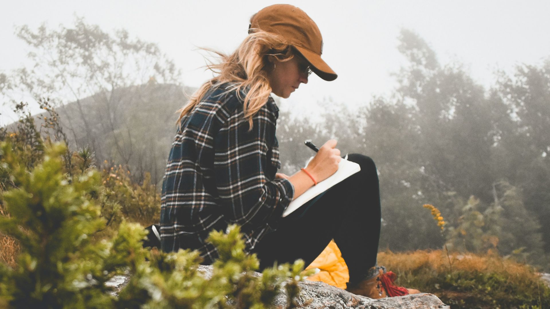a woman sitting on top of a rock writing