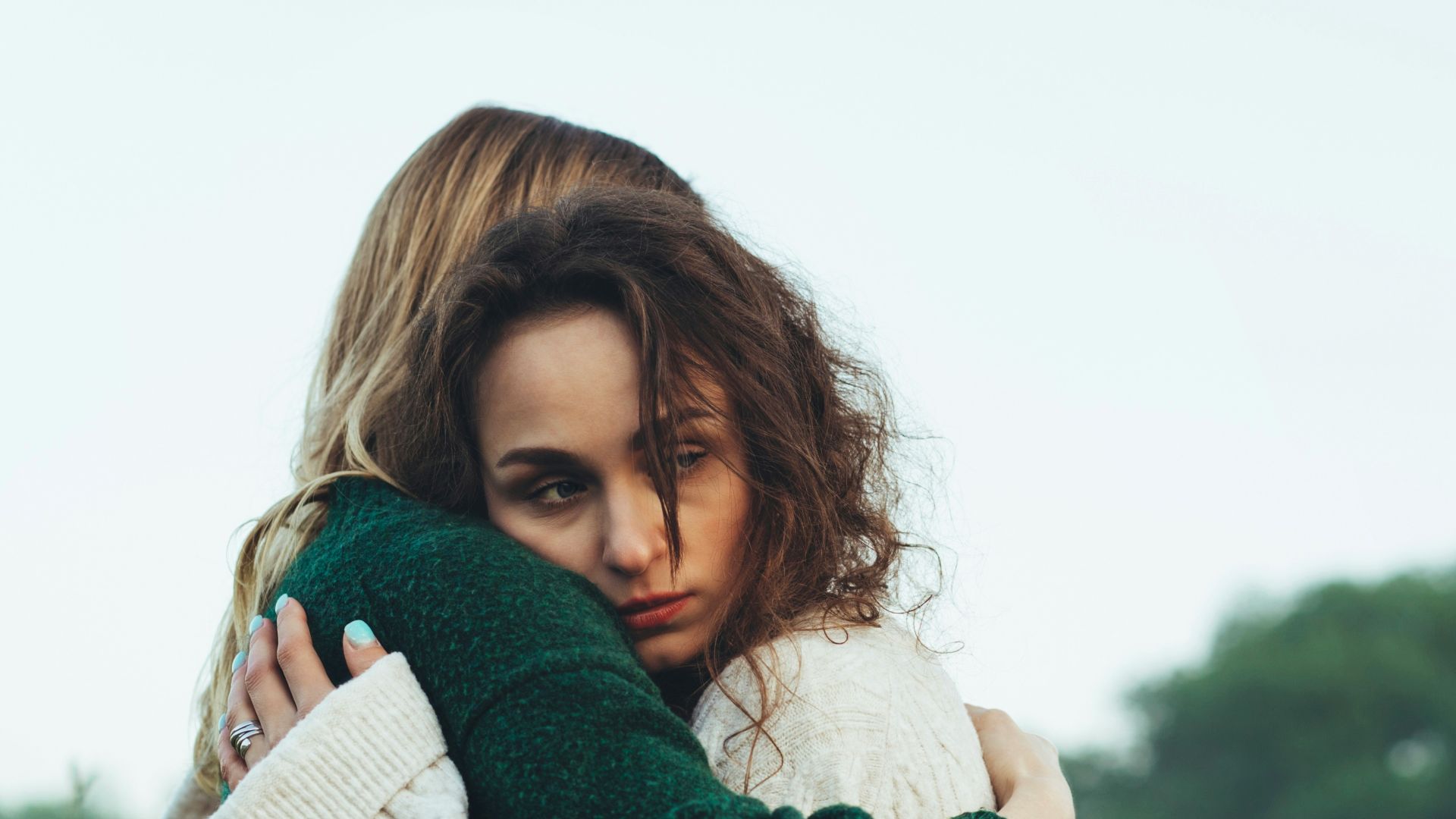 a woman in a green and white sweater hugging a woman in a green and white