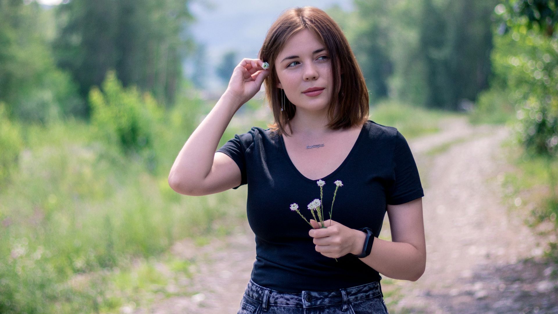 A woman holds flowers while outdoors on a trail.